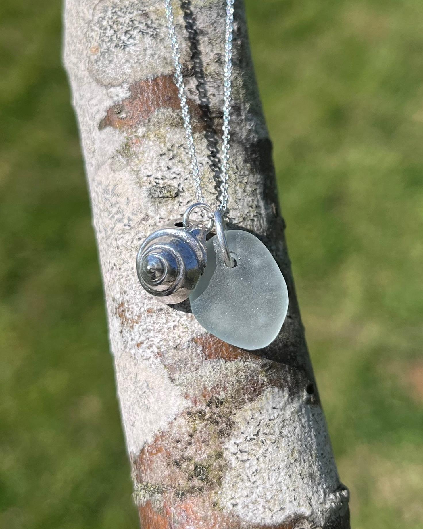 Necklace with a silver shell and seaglass pendant laid on a tree branch