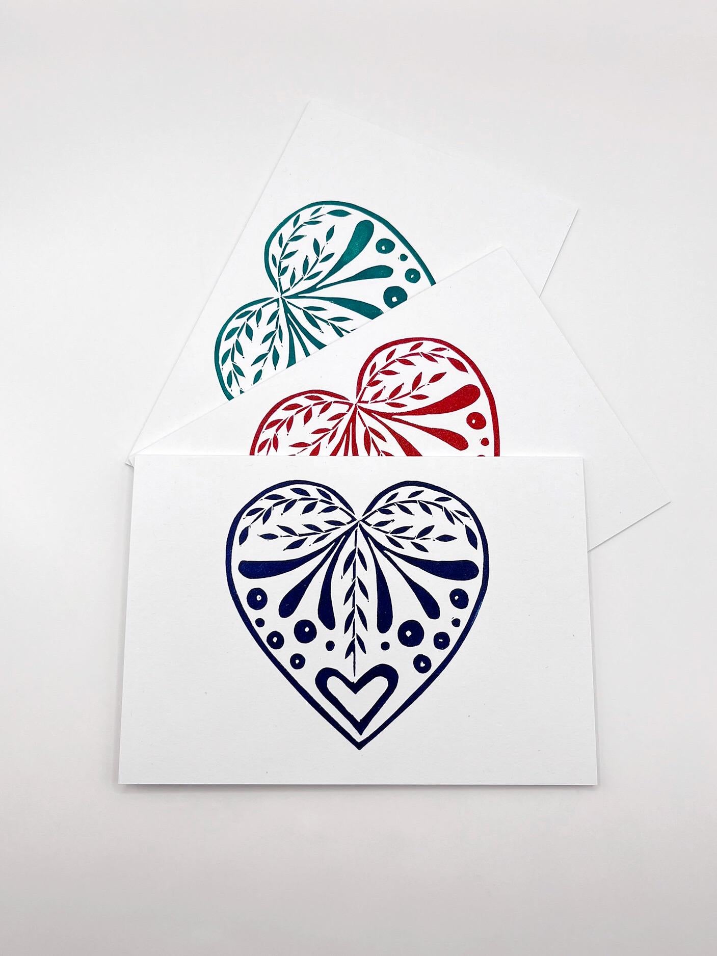 Set of three white cards with original lino printed heart designs. Laid on a white surface. 