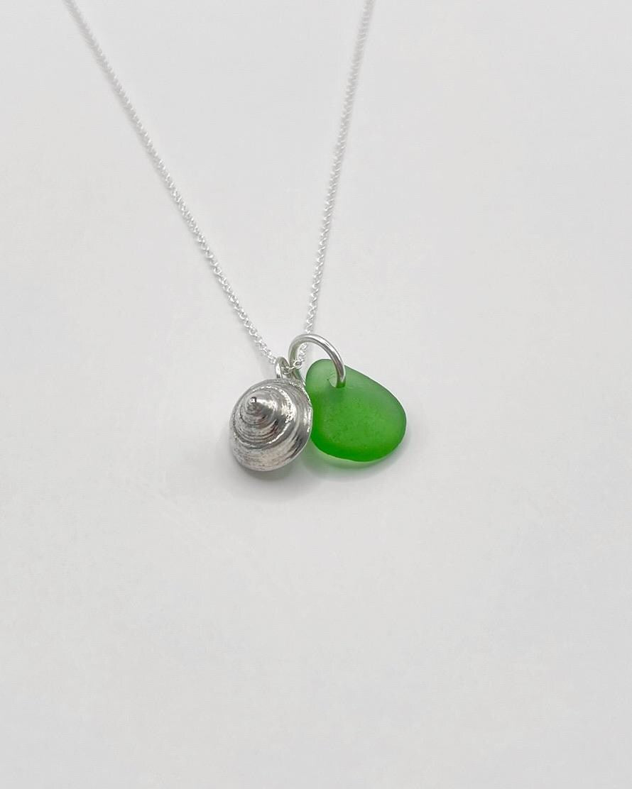Necklace with a silver shell and green sea glass laid on a white background