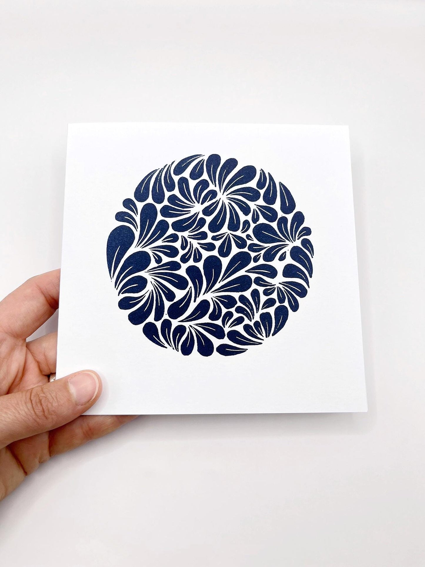 Hand holding a card with a blue original lino print mussel shell pattern on a white background