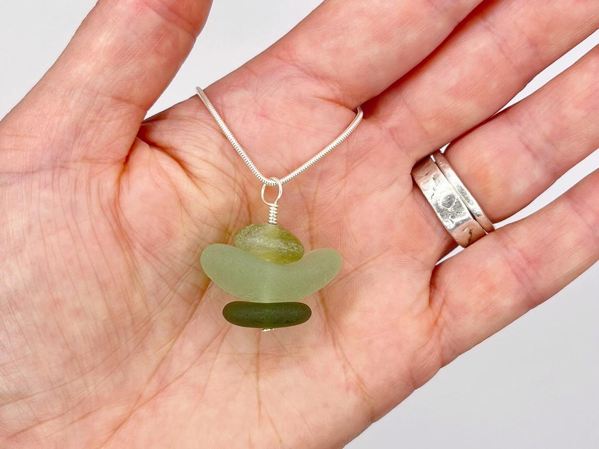 Hand holding a green sea glass and Jade  pendant on a silver chain against a white background