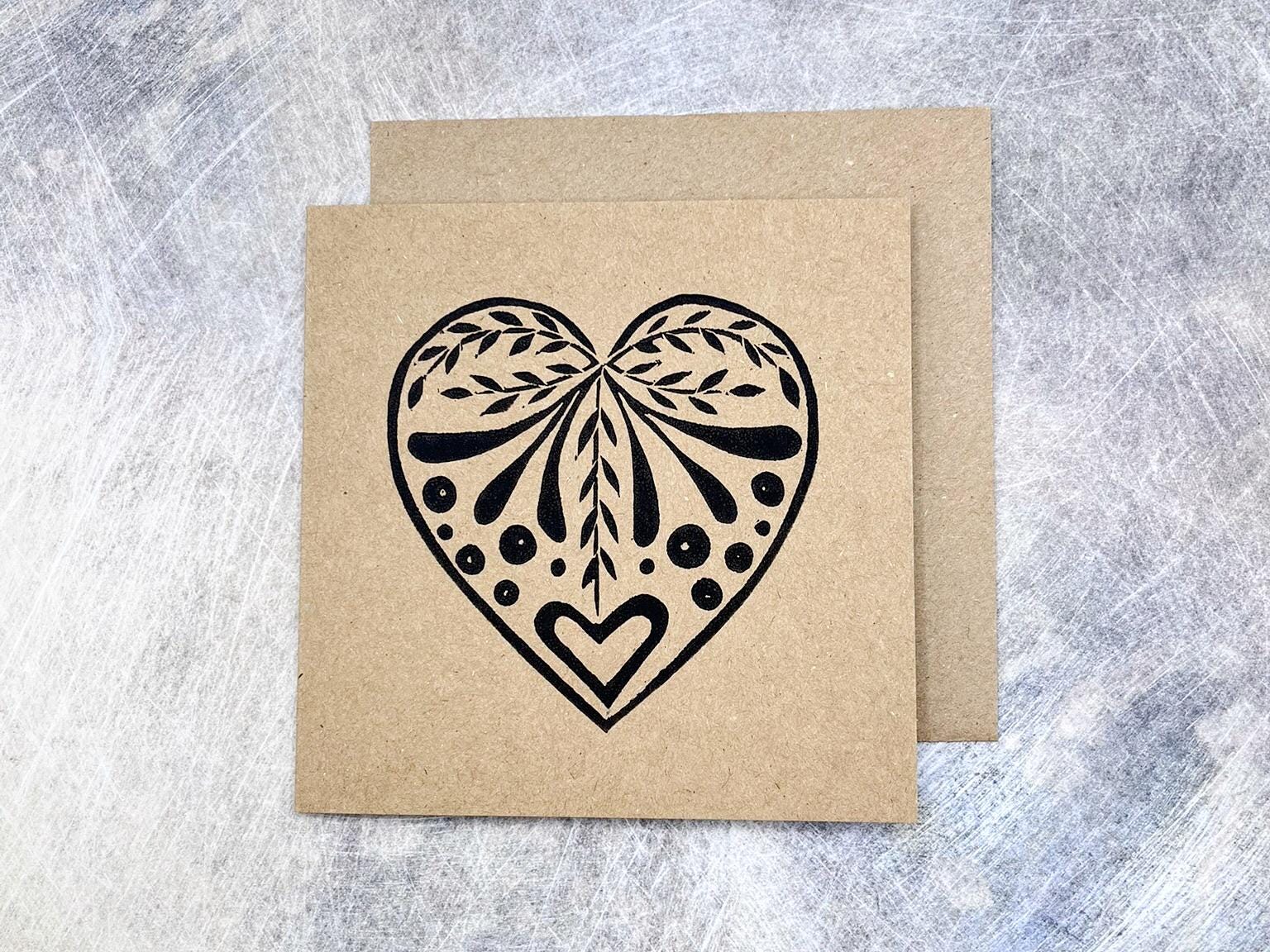 Card with an original lino printed black heart design on Kraft card with matching envelope, laid on a textured surface. 
