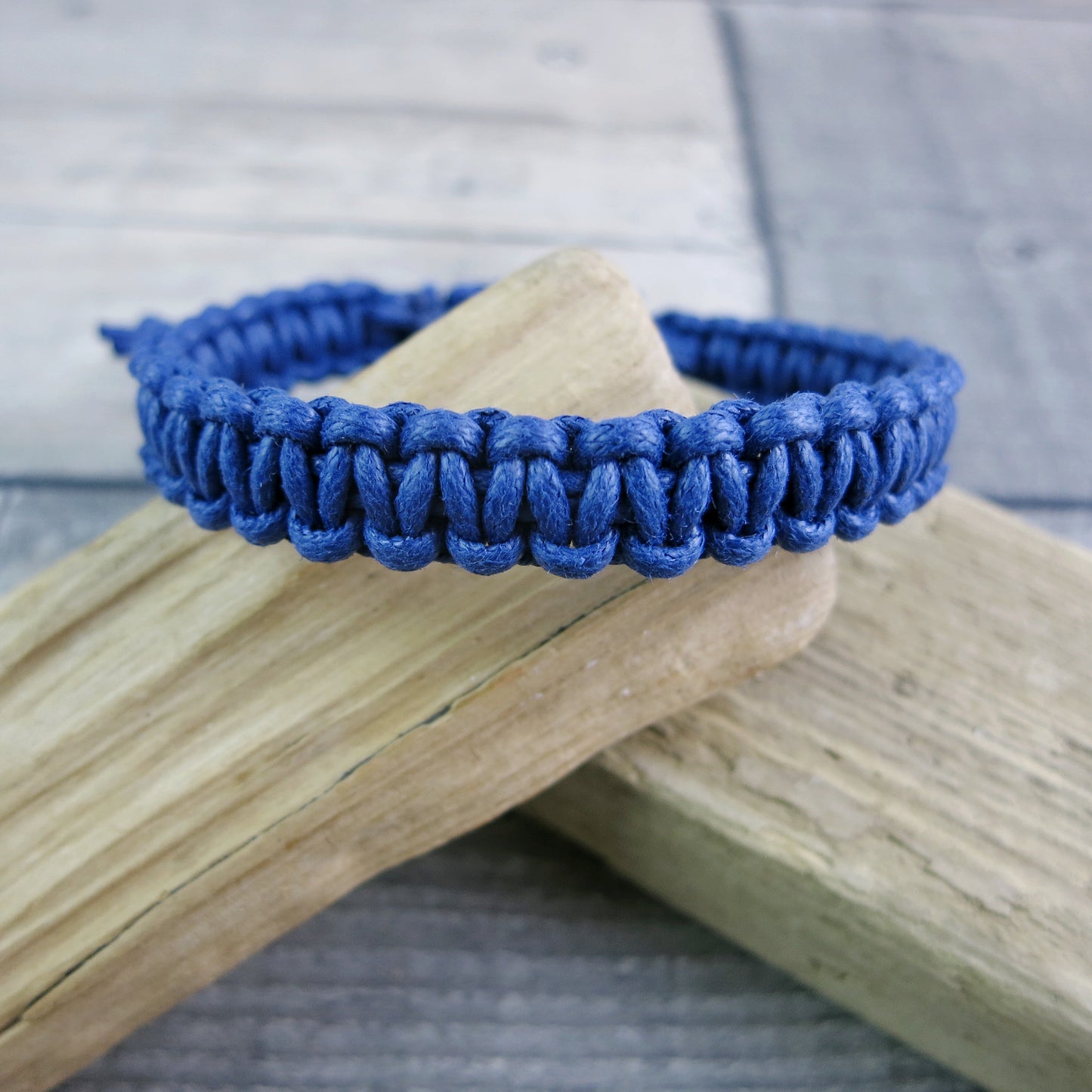 Blue macrame bracelet laid on driftwood against a textured background