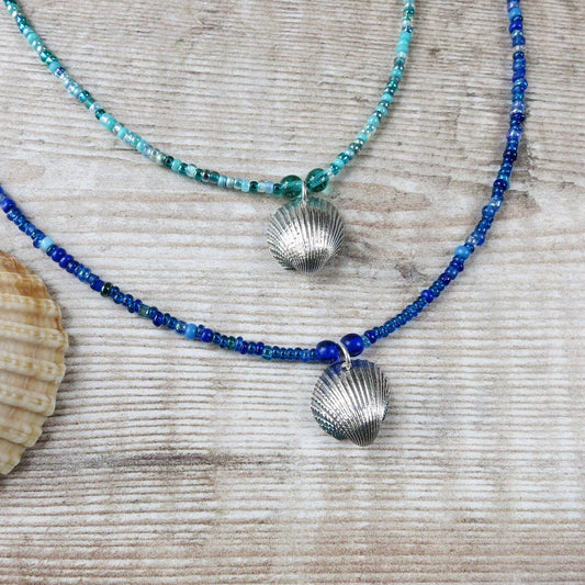 Two seed bead necklaces with silver coated shell pendants laid on a textured surface