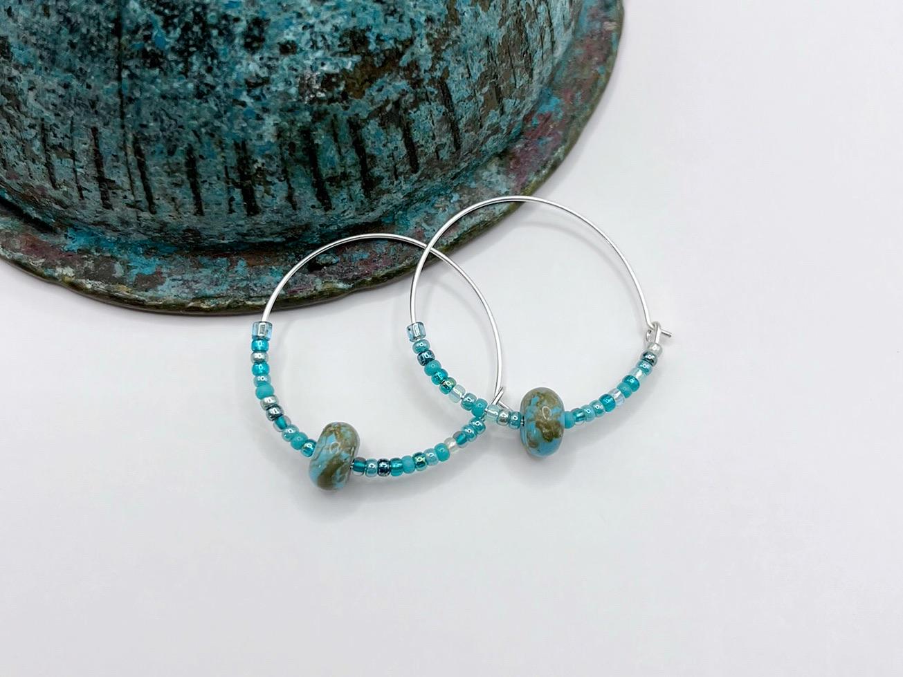 Pair of silver hoop earrings with turquoise beads laid on a white background
