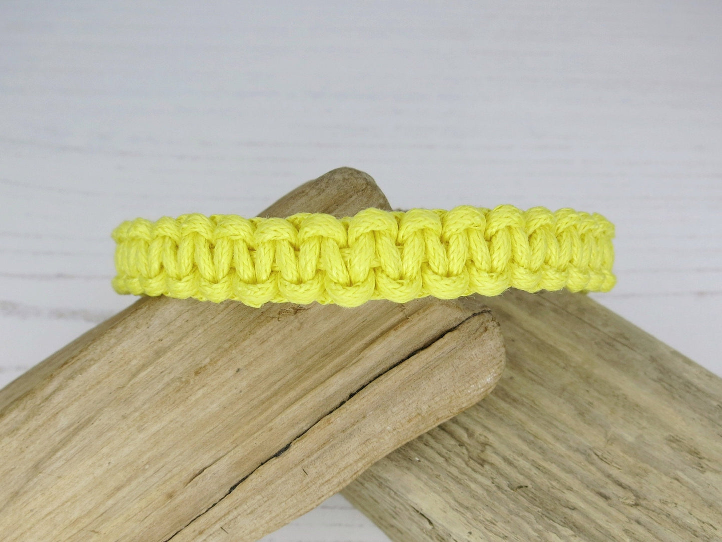 Yellow macrame bracelet on a wooden surface with a white background