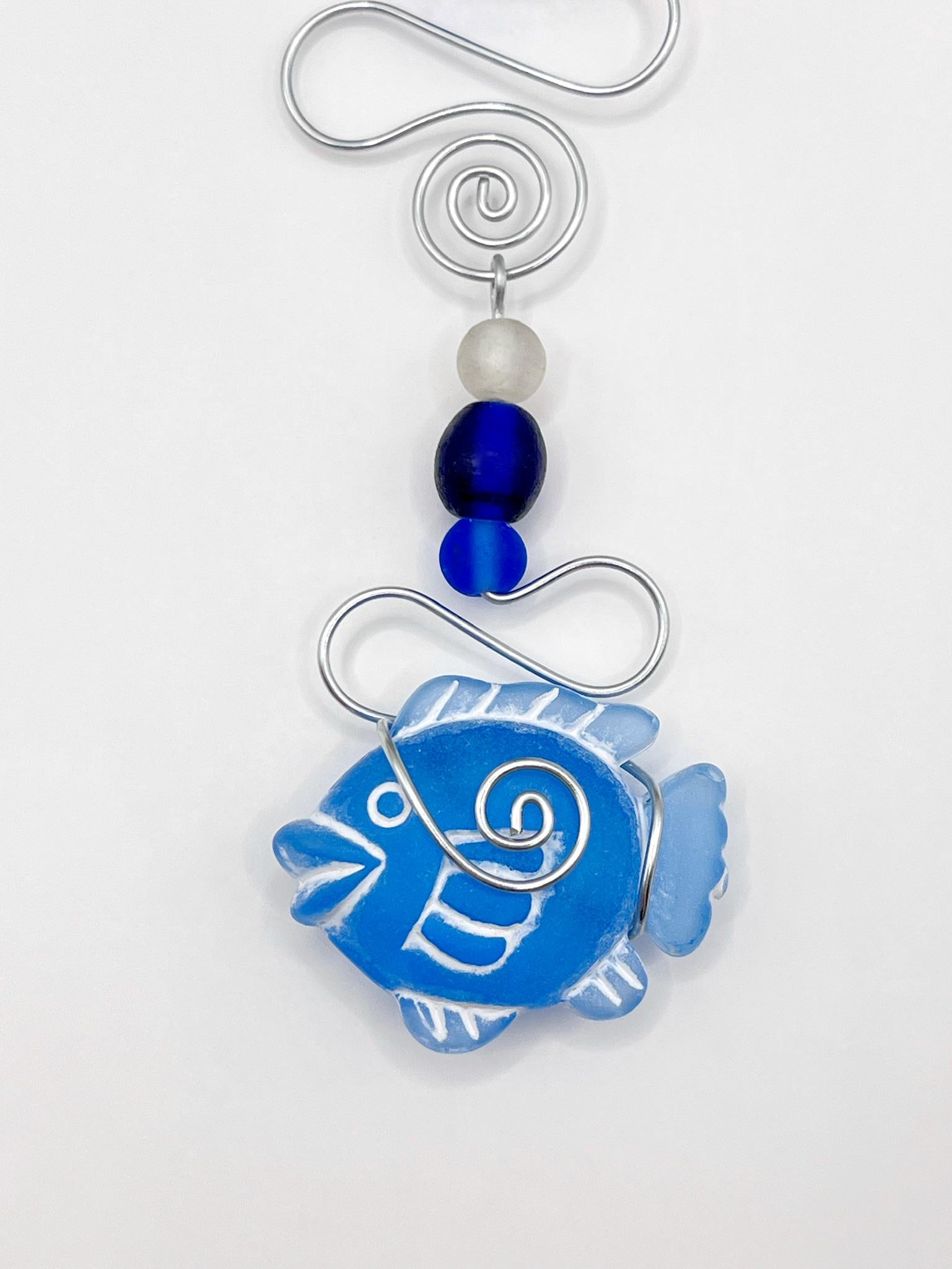 Close up of decorative hanging ornament with blue fish design, wire and glass beads on a white background