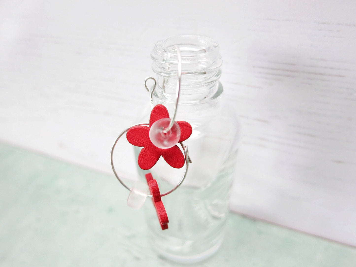 Close up of silver hoop earrings with Blue wooden flowers and a glass bead hanging on a glass bottle 