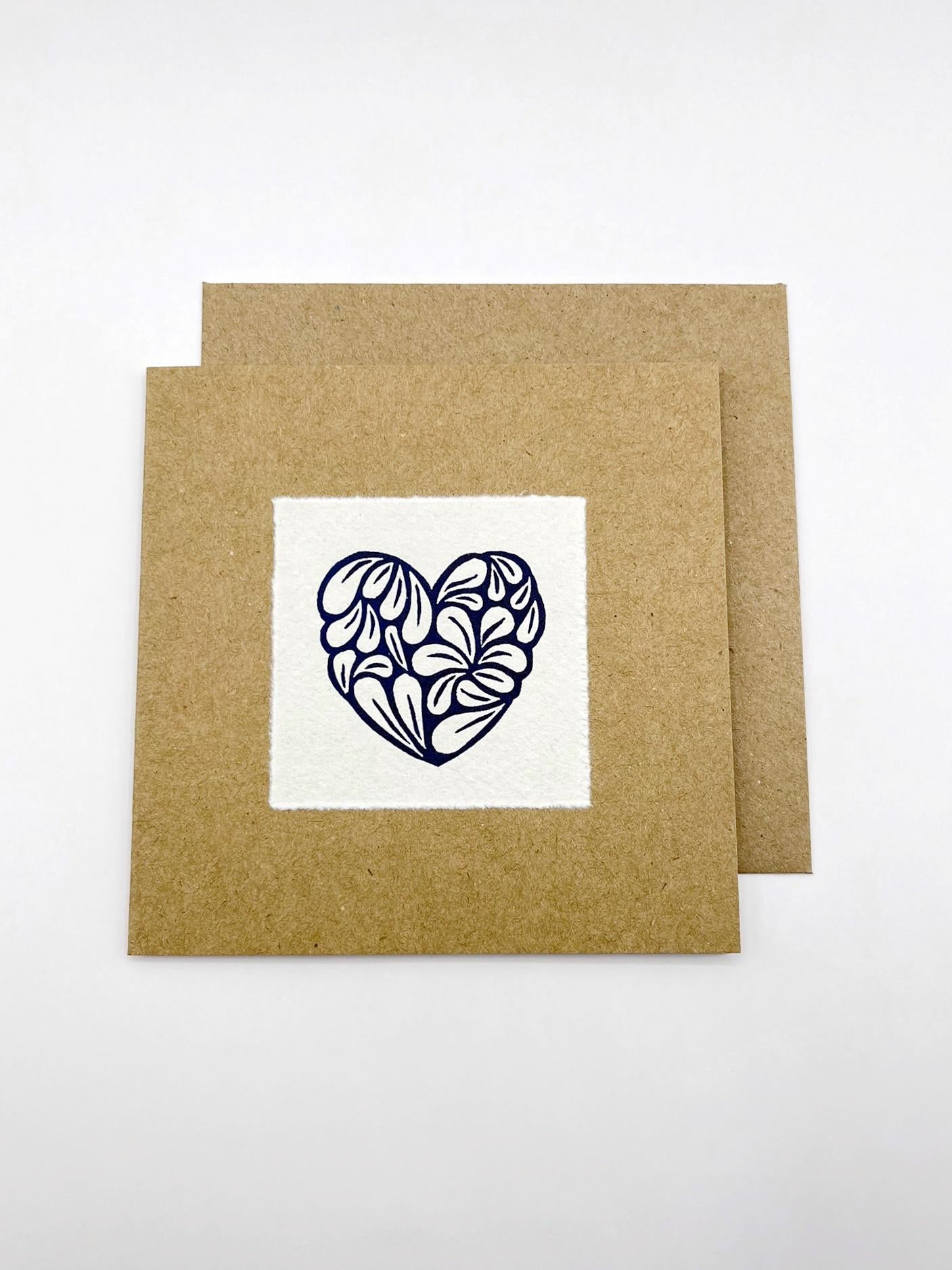 Kraft card with a white square featuring an original lino printed blue heart design with matching Kraft envelope, laid on a white background.