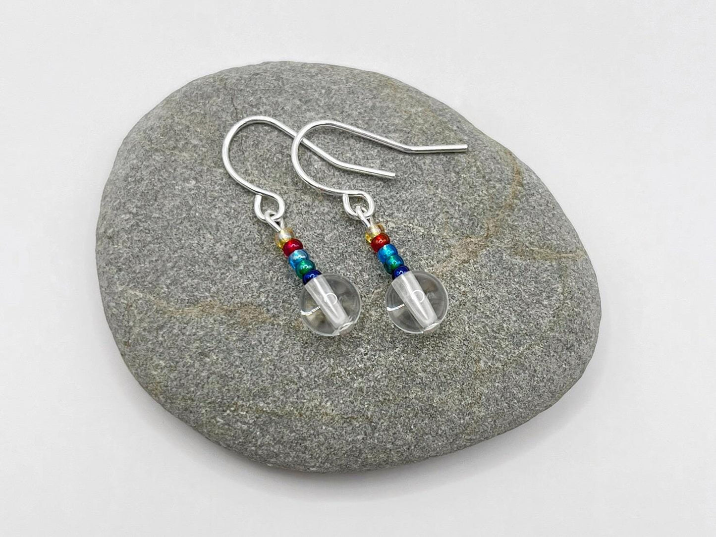 Pair of earrings with clear crystal and rainbow seed beads laid on a grey stone
