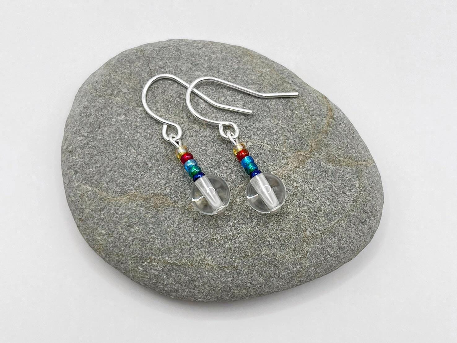 Pair of earrings with clear crystal and rainbow seed beads laid on a grey stone