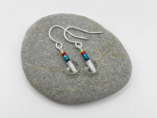 Pair of earrings with clear crystal and rainbow seed beads laid on a grey stone