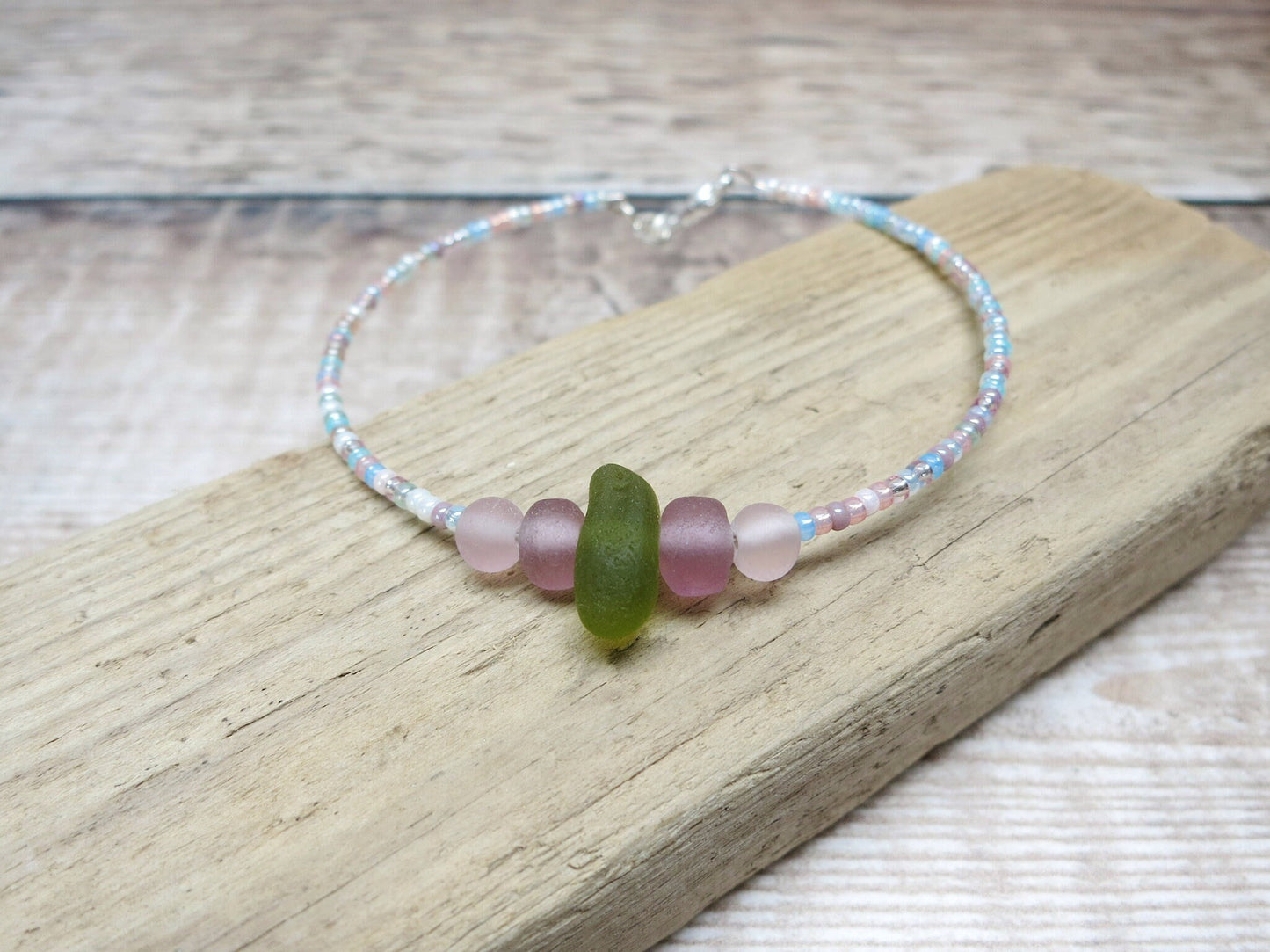 Pastel seed beaded bracelet with olive green sea glass laid on driftwood