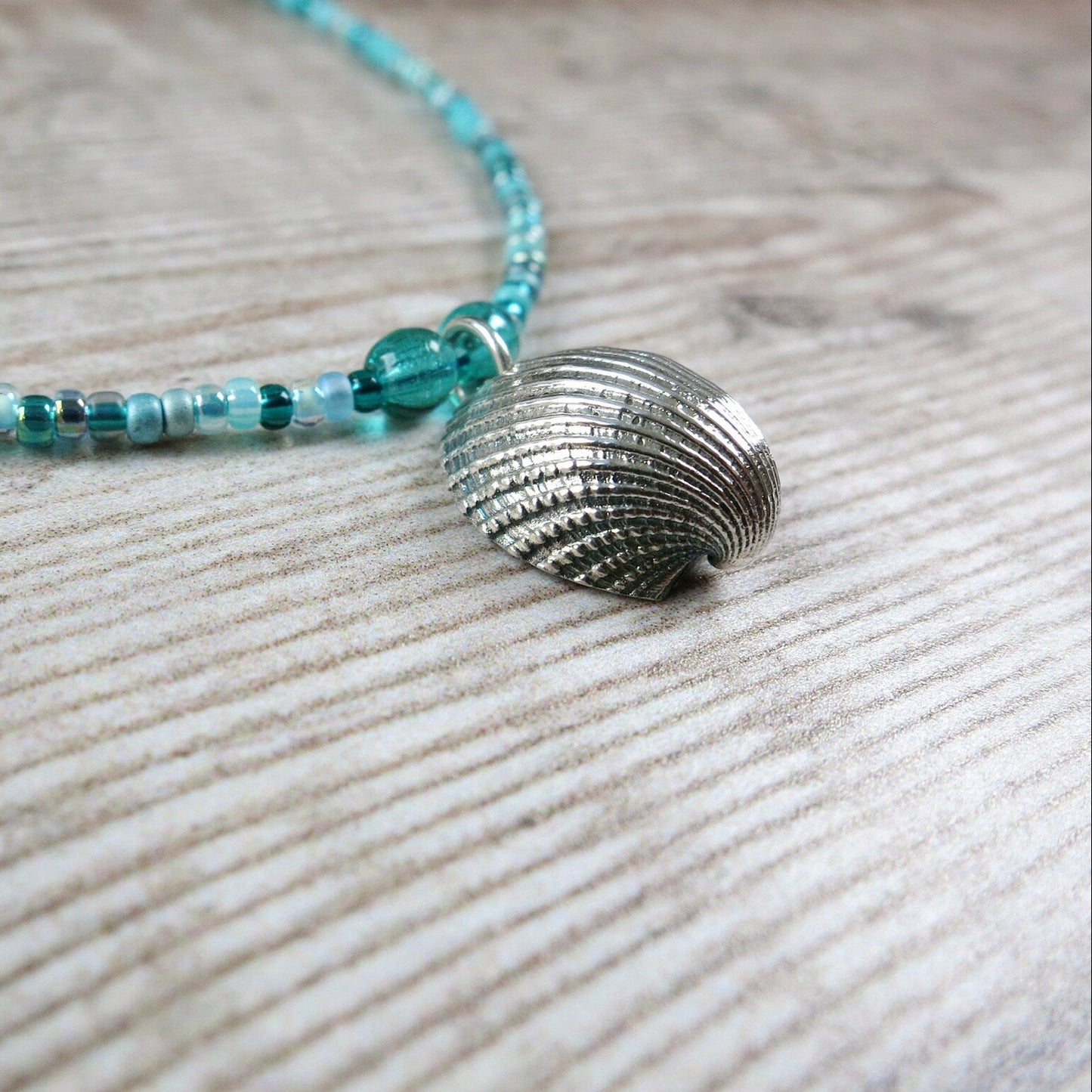 Close up of turquoise seed bead necklace  with silver shell pendant laid on a textured surface