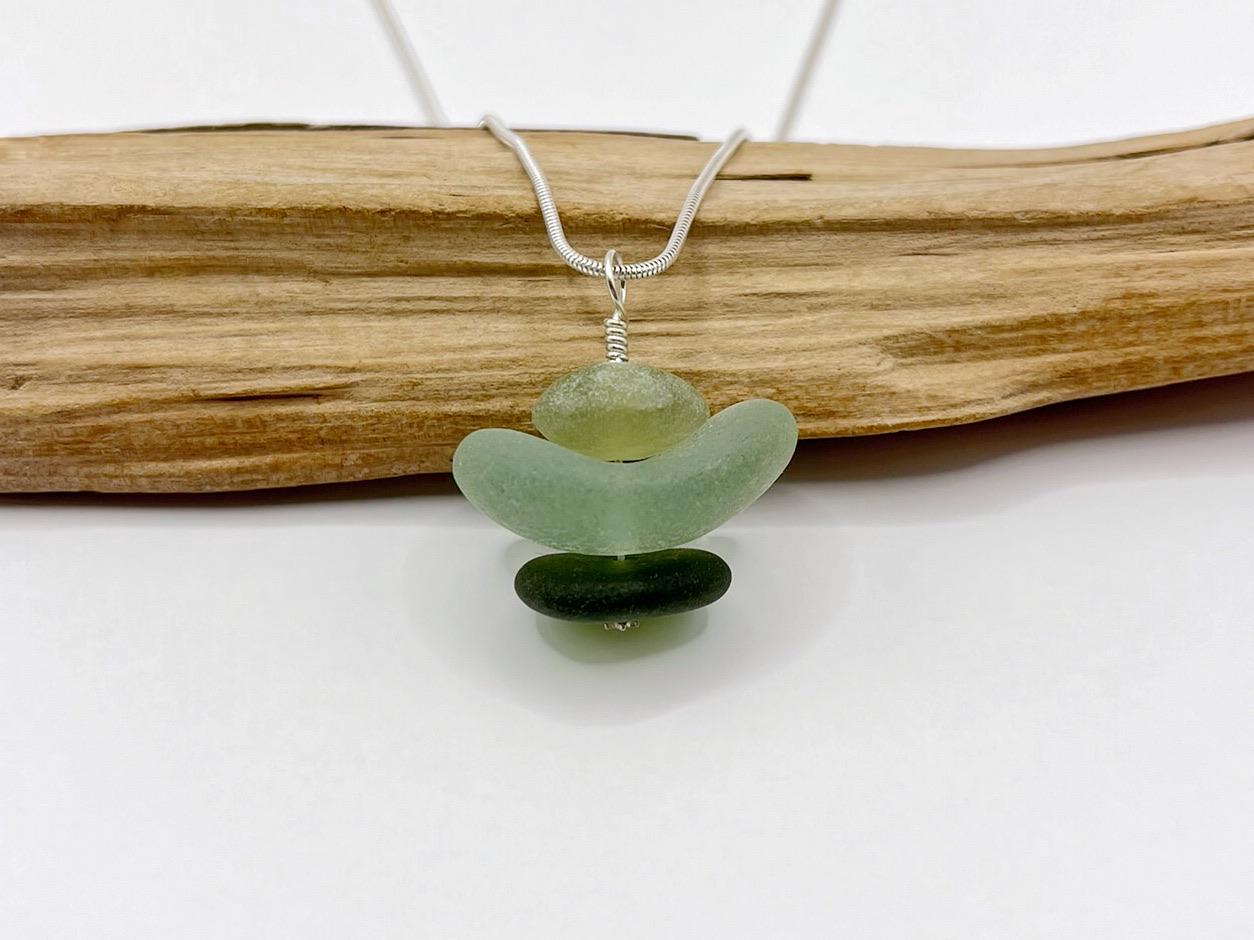 Necklace with green sea glass and Jade pendant sat against driftwood on a white background
