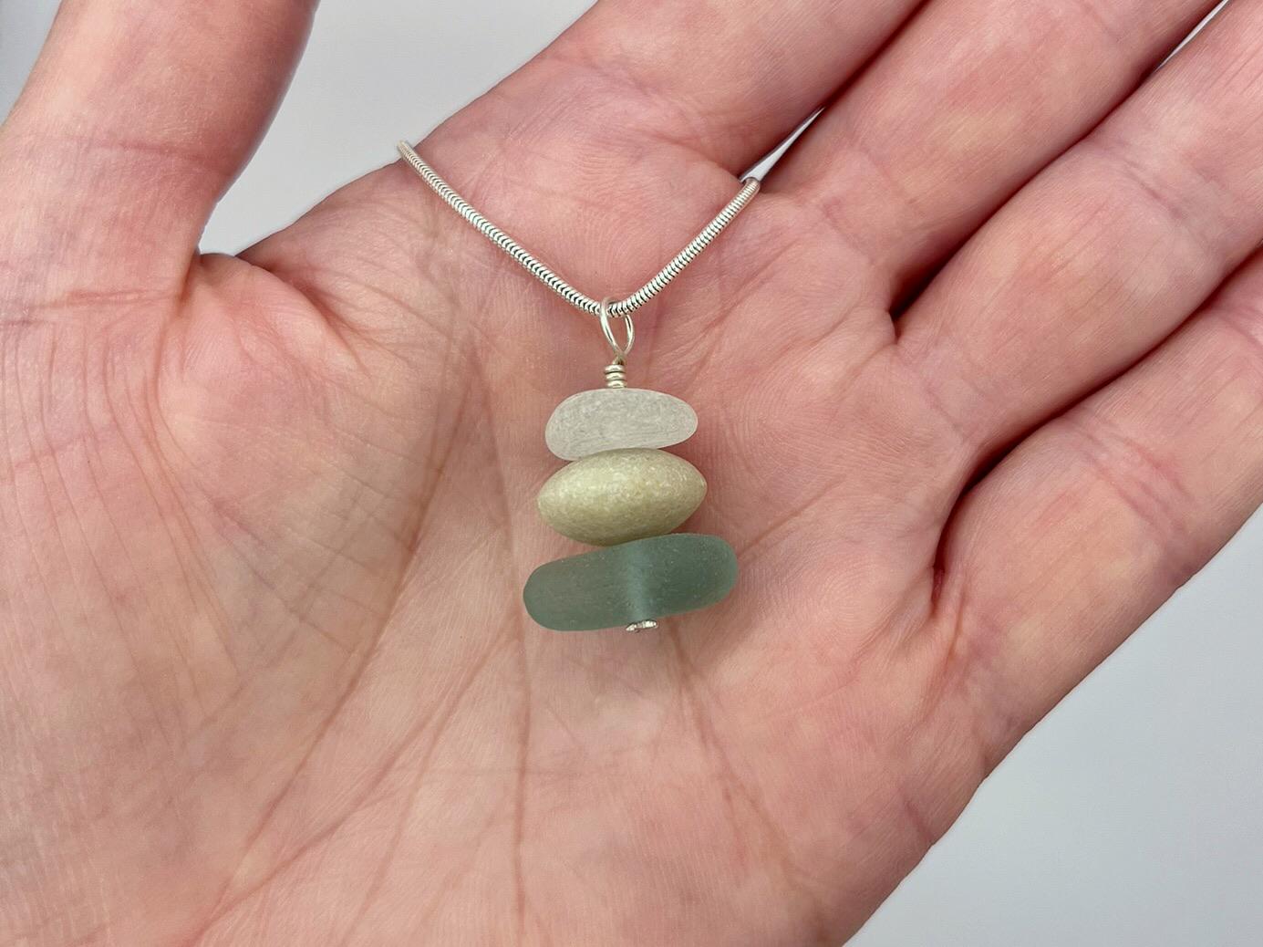 Hand holding a necklace with three layered stones on a plain background