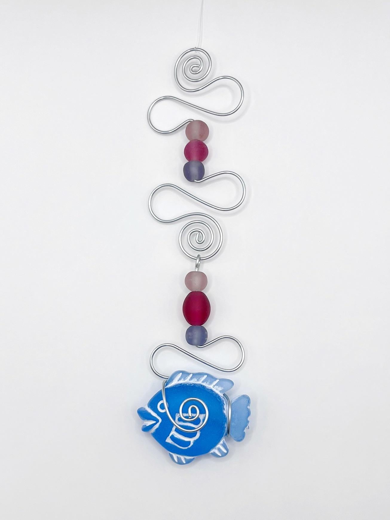 Decorative ornament with blue fish, wire and colourful beads on a white background