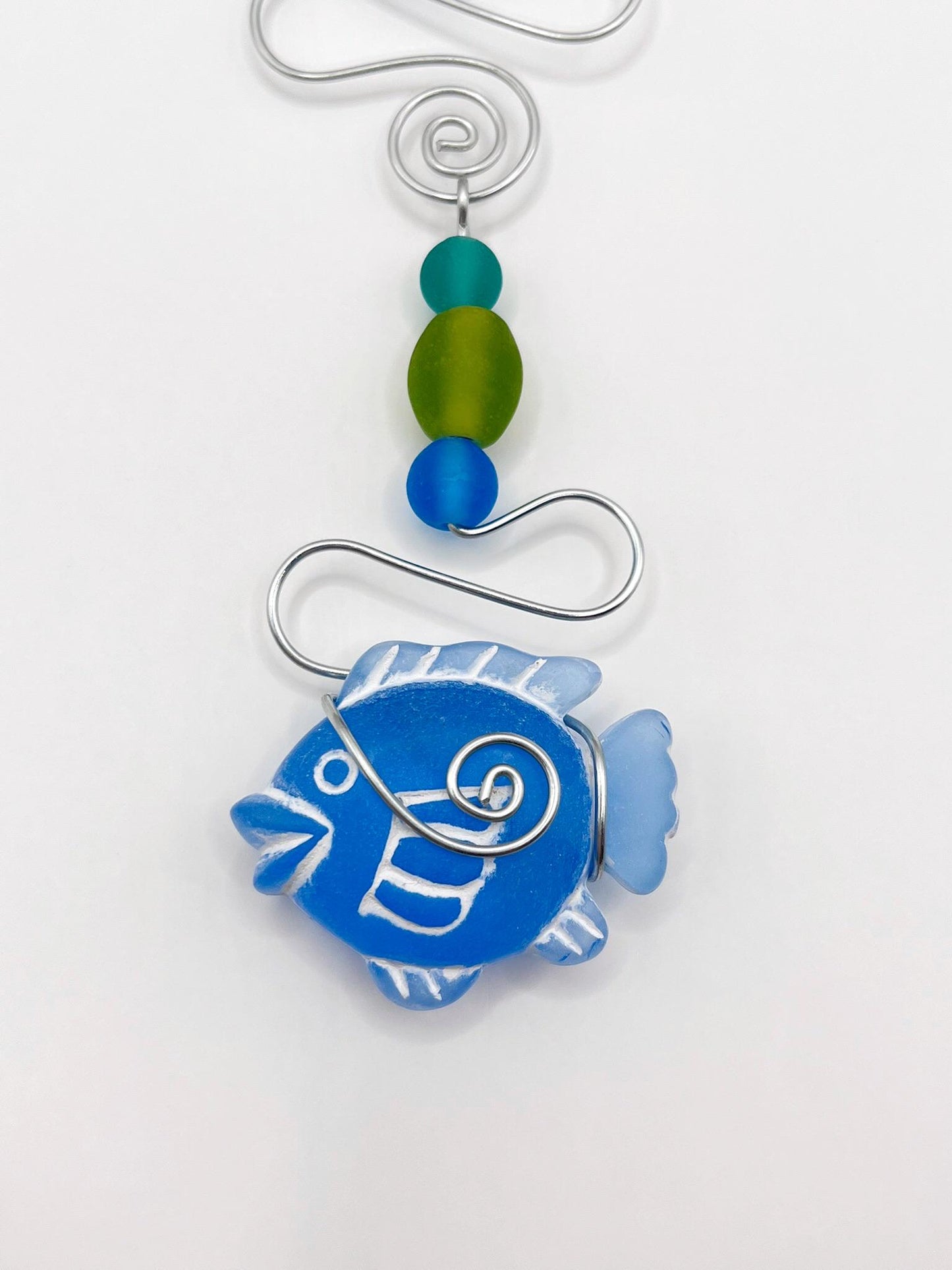 Close up of decorative hanging ornament with blue fish, wire and colourful beads on a white background