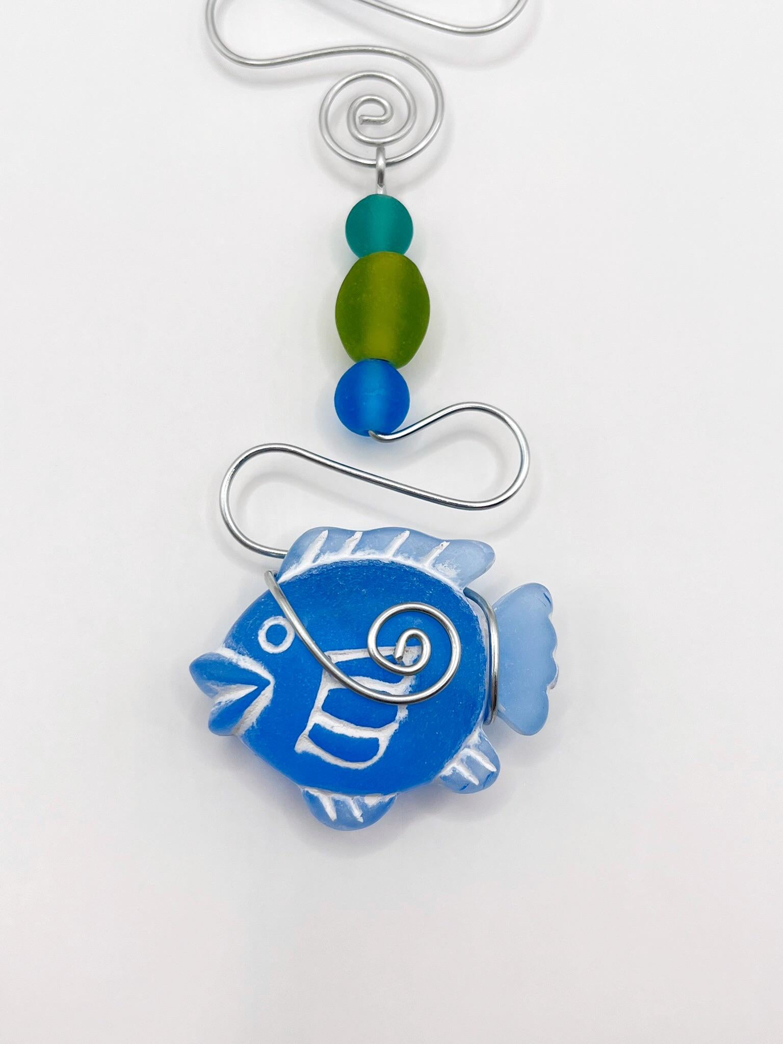Close up of decorative hanging ornament with blue fish, wire and colourful beads on a white background