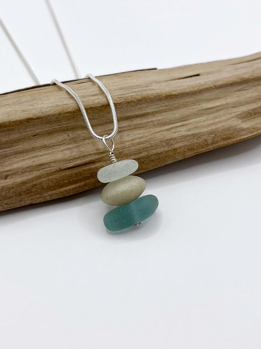 Necklace with stacked sea glass leant against driftwood on a white background