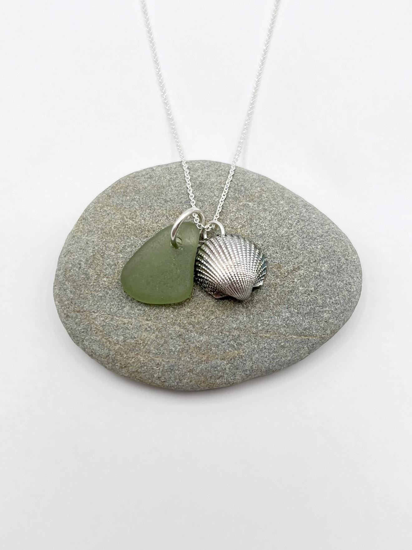 Necklace with green sea glass and a silver shell laid on a grey pebble