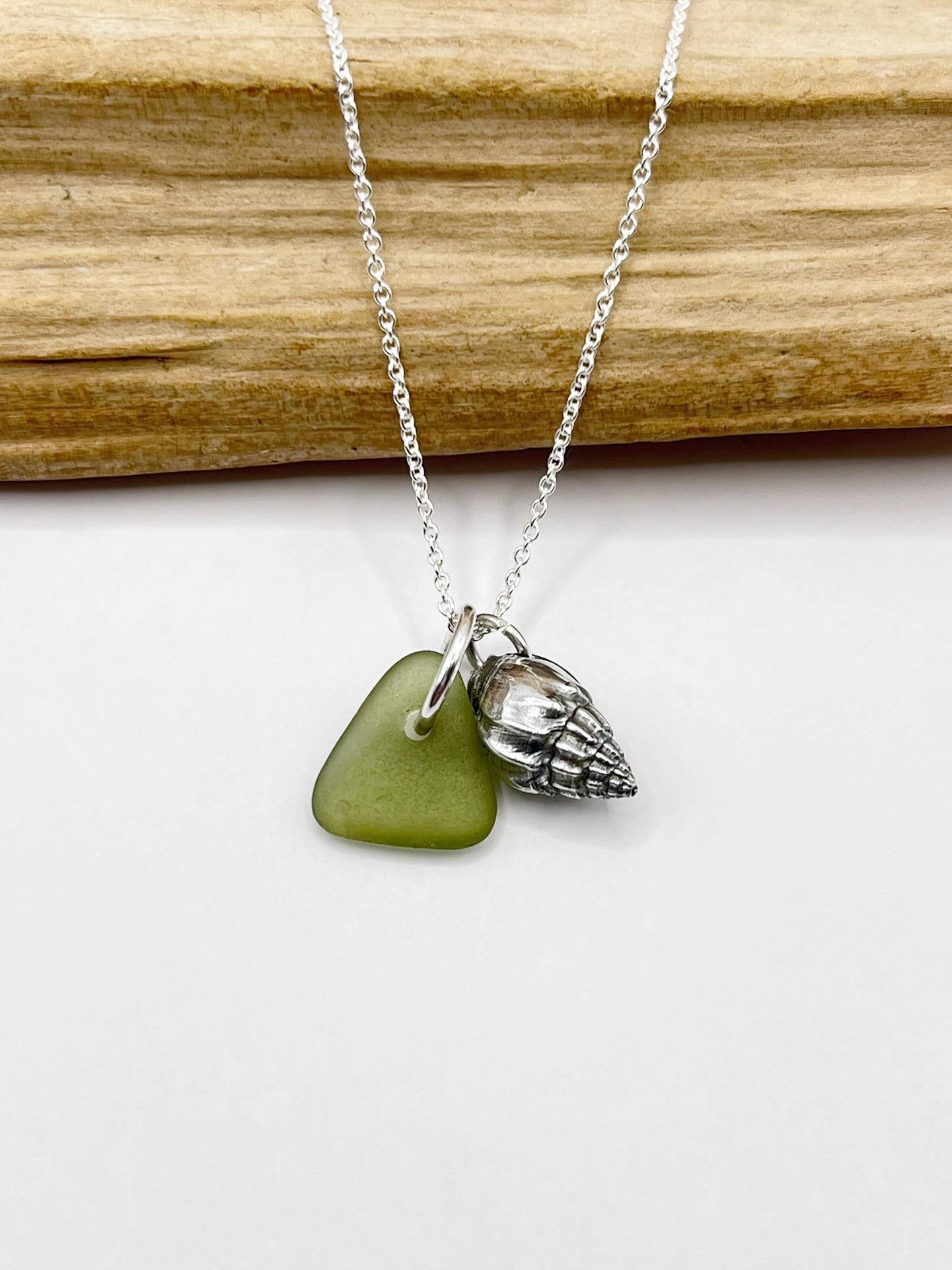 Necklace with olive green sea glass and a silver shell laid on driftwood