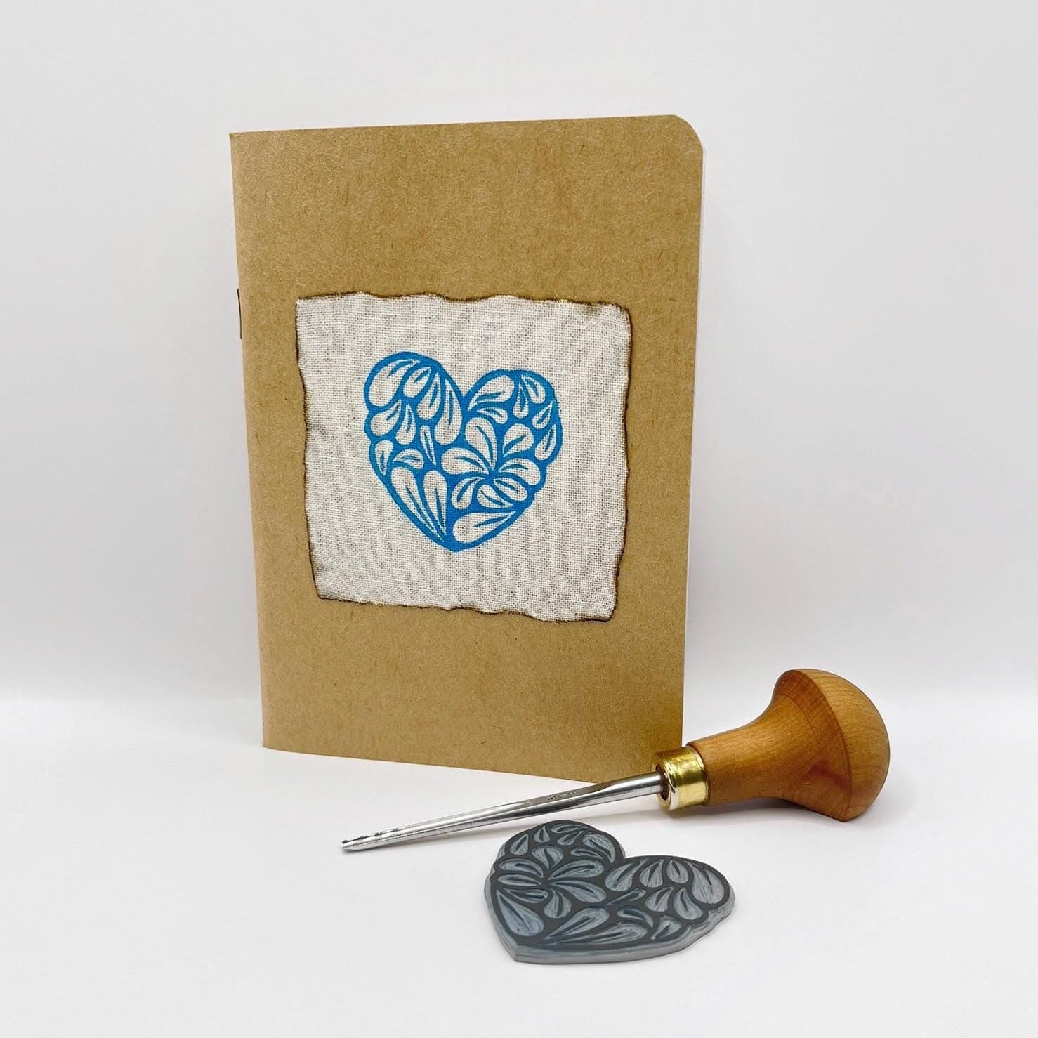 Card with a blue heart design, lino, and cutting tool on a white background