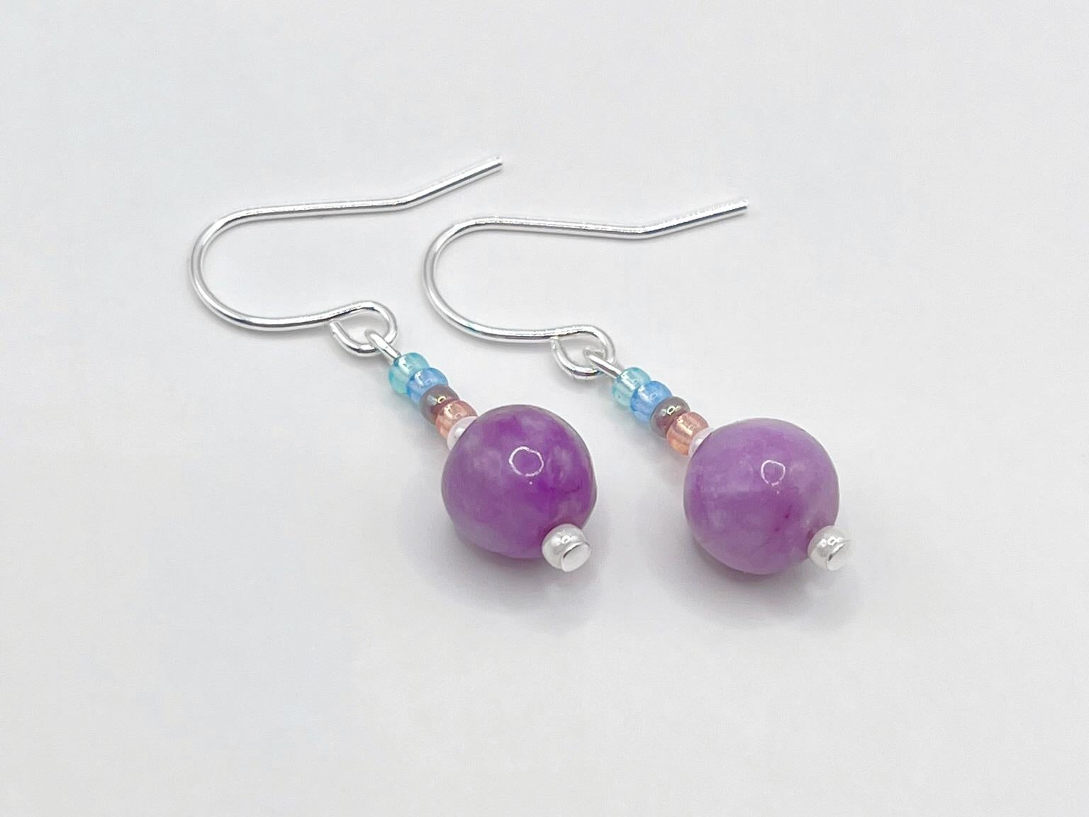 Close up of a pair of pastel seed bead and lilac jasper earrings laid on a white background.