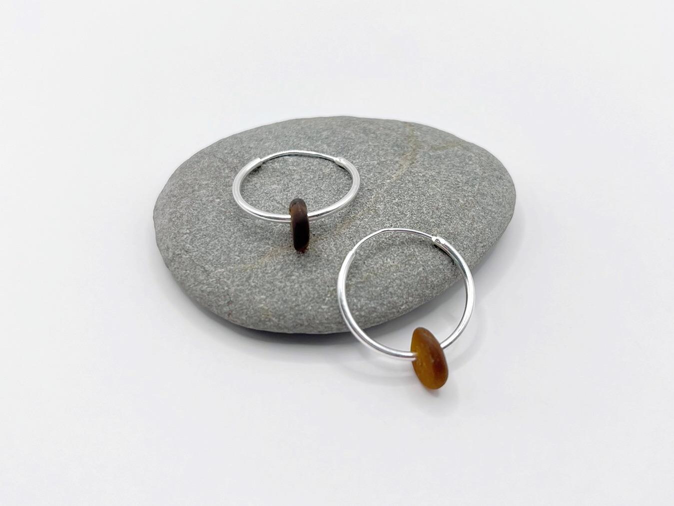 Silver hoop earrings with burnt orange sea glass on a grey pebble against a white background