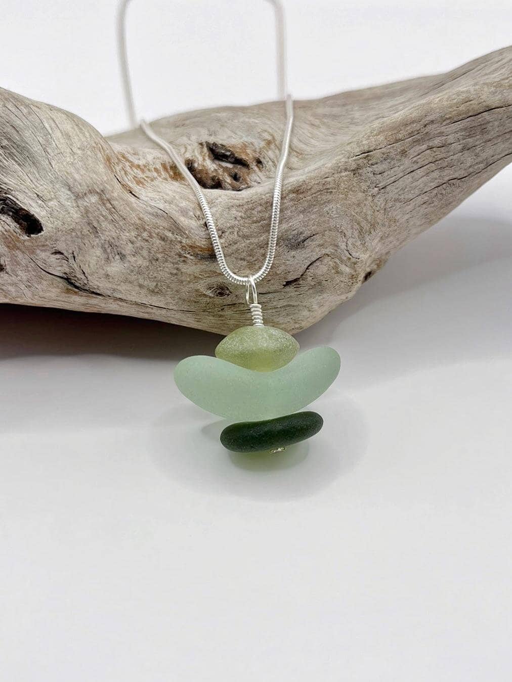 Necklace with green sea glass and Jade pendant sat against driftwood on a white background