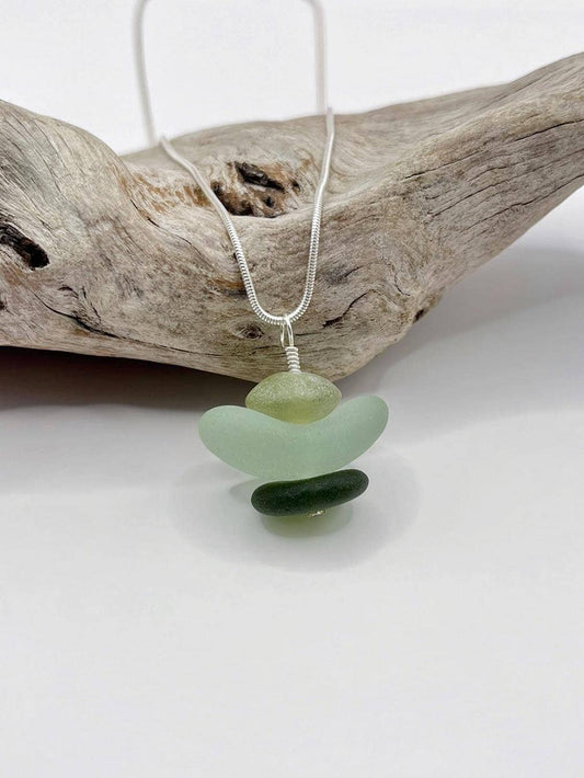 Necklace with green sea glass and Jade pendant sat against driftwood on a white background