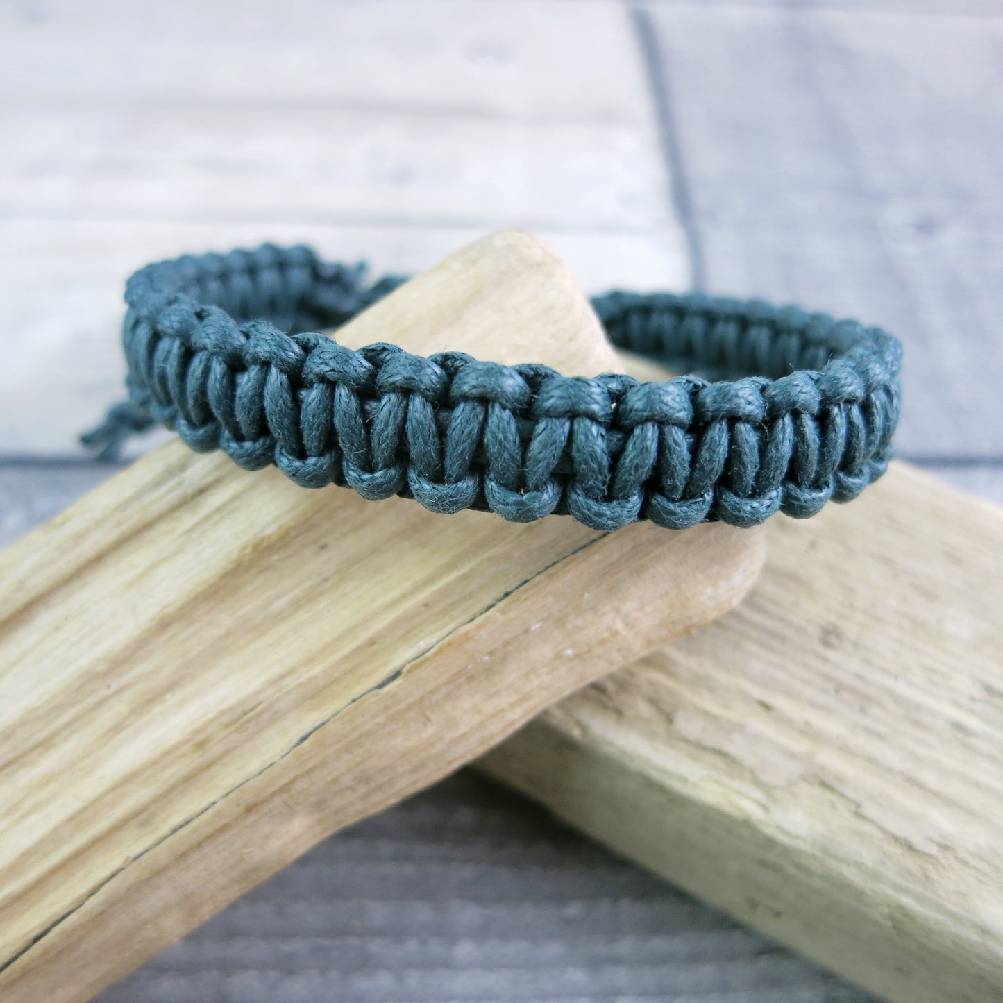 Green macrame bracelet laid on driftwood against a textured background.