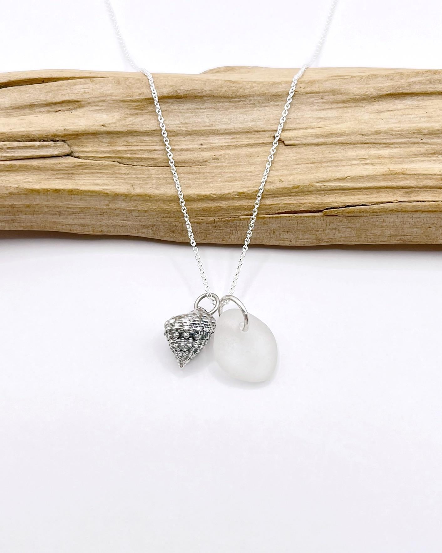 Silver necklace with White Sea glass and silver shell pendant laid in front of driftwood against a white background