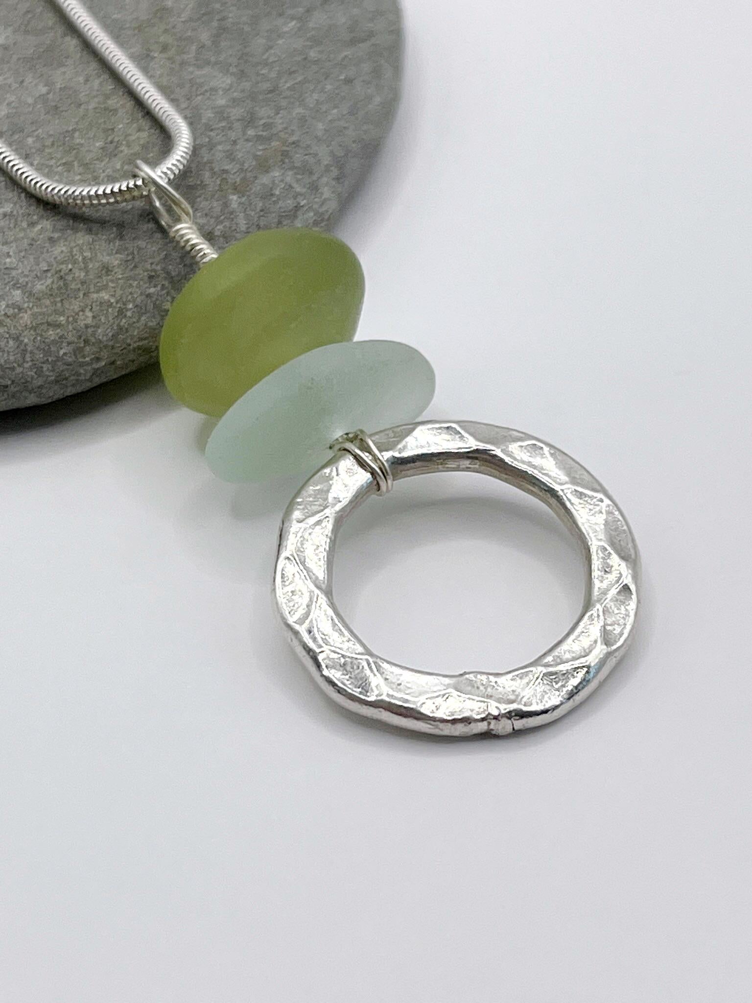 Close up of silver necklace with a textured silver ring pendant, green Jade and sea glass on a grey background