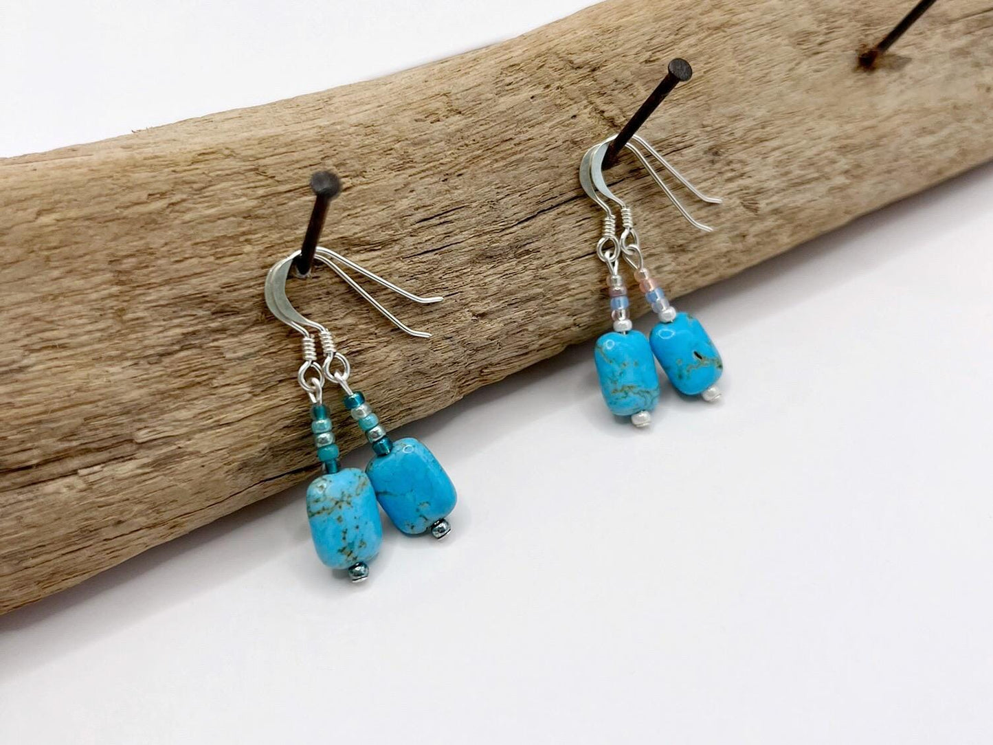 Turquoise beaded earrings hanging on a piece of driftwood.