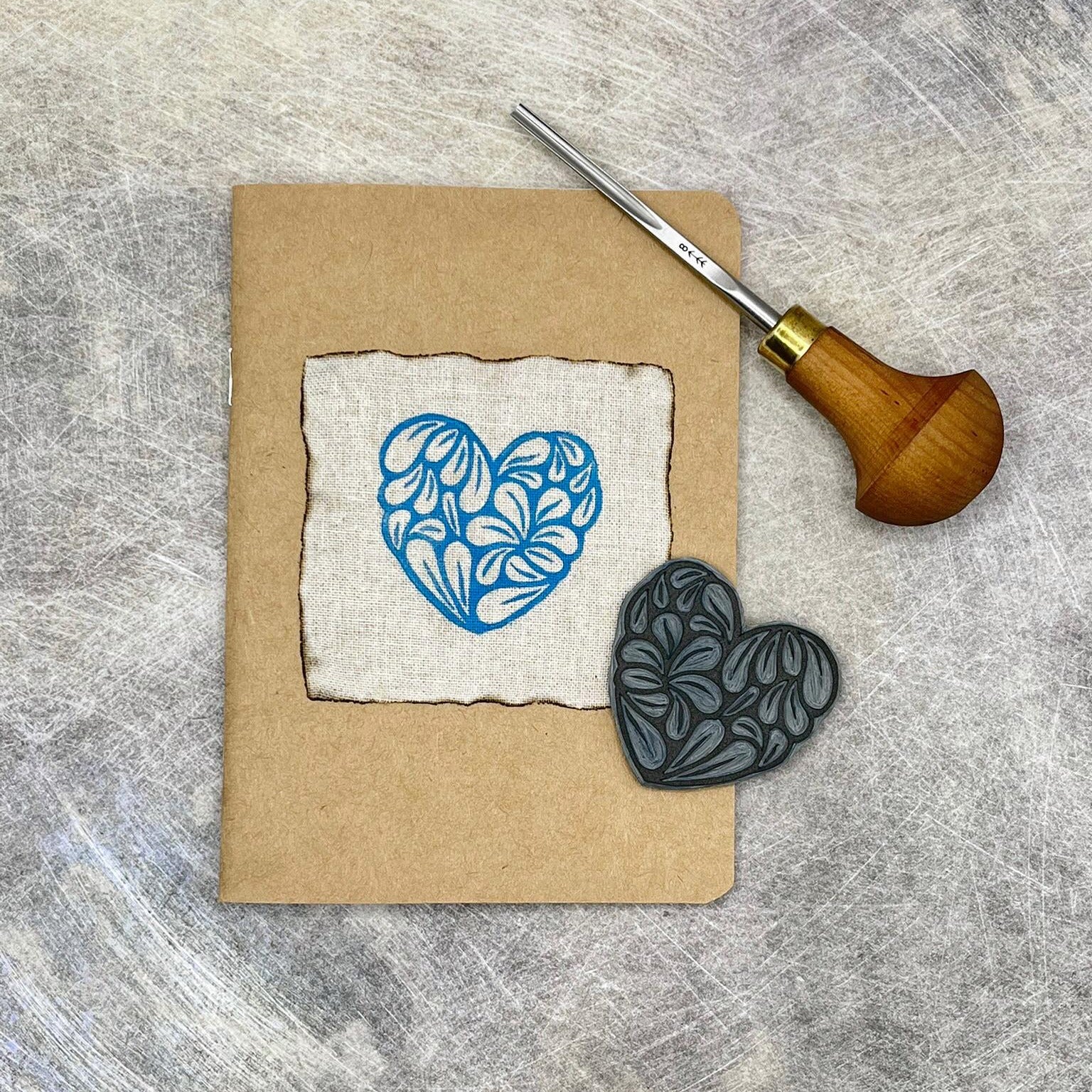 A6 Kraft sketchbook with original heart lino print, lino and carving tool on a textured surface