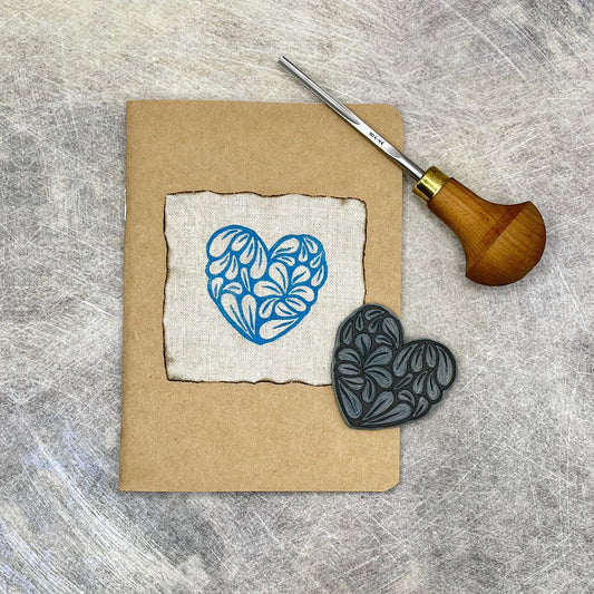 A6 Kraft sketchbook with original heart lino print, lino and carving tool on a textured surface