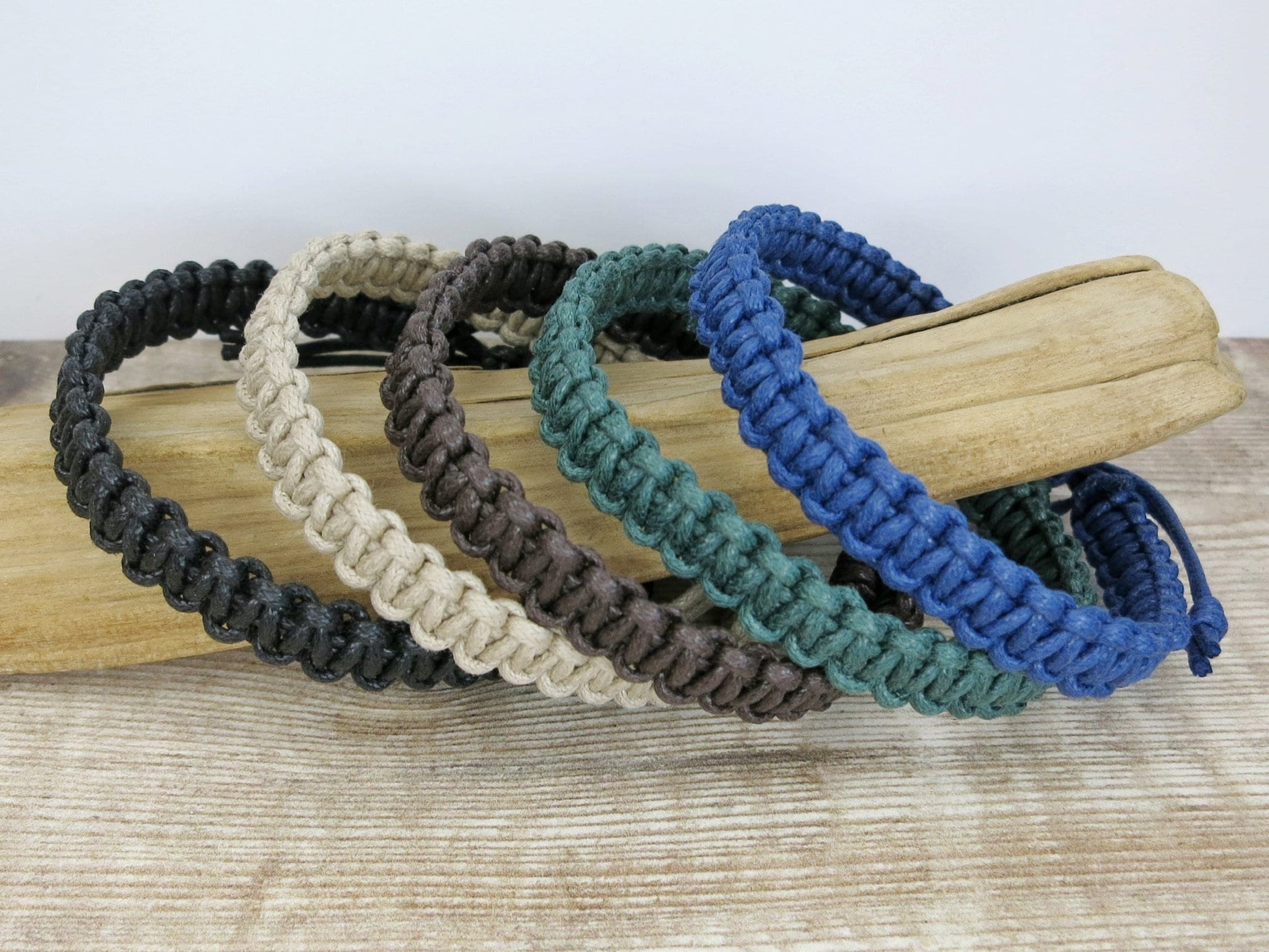 Set of five macrame bracelets in black, natural, brown, green, and blue on a piece of driftwood.