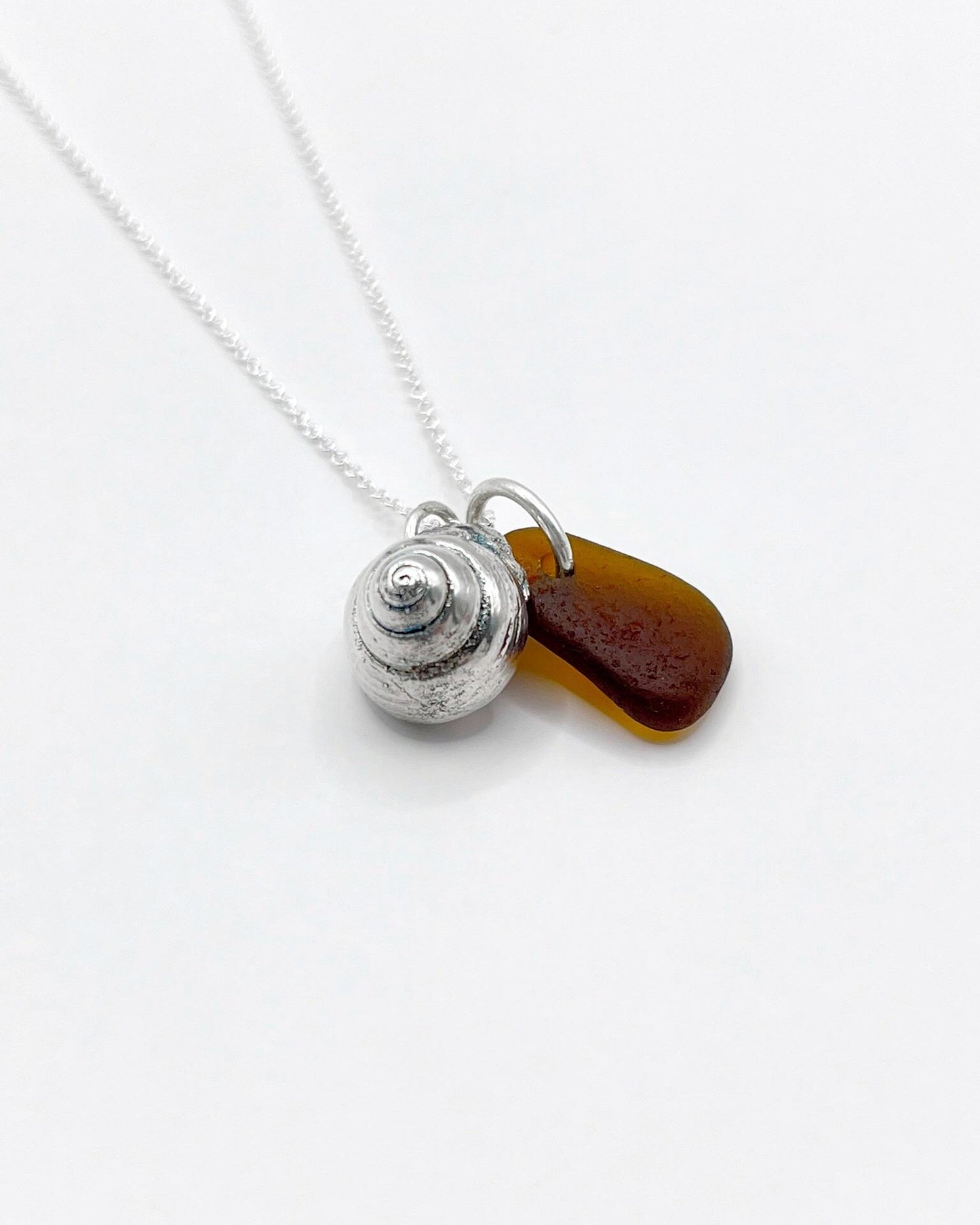 Silver necklace with burnt orange sea glass and a silver shell pendant laid on a white background