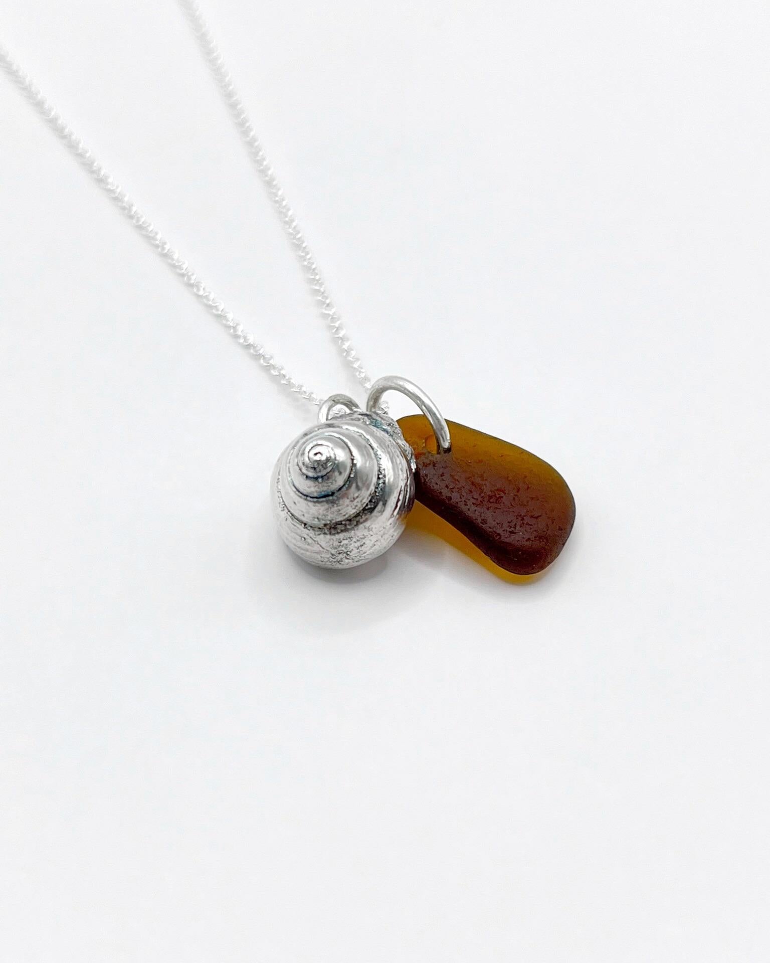 Silver necklace with burnt orange sea glass and a silver shell pendant laid on a white background