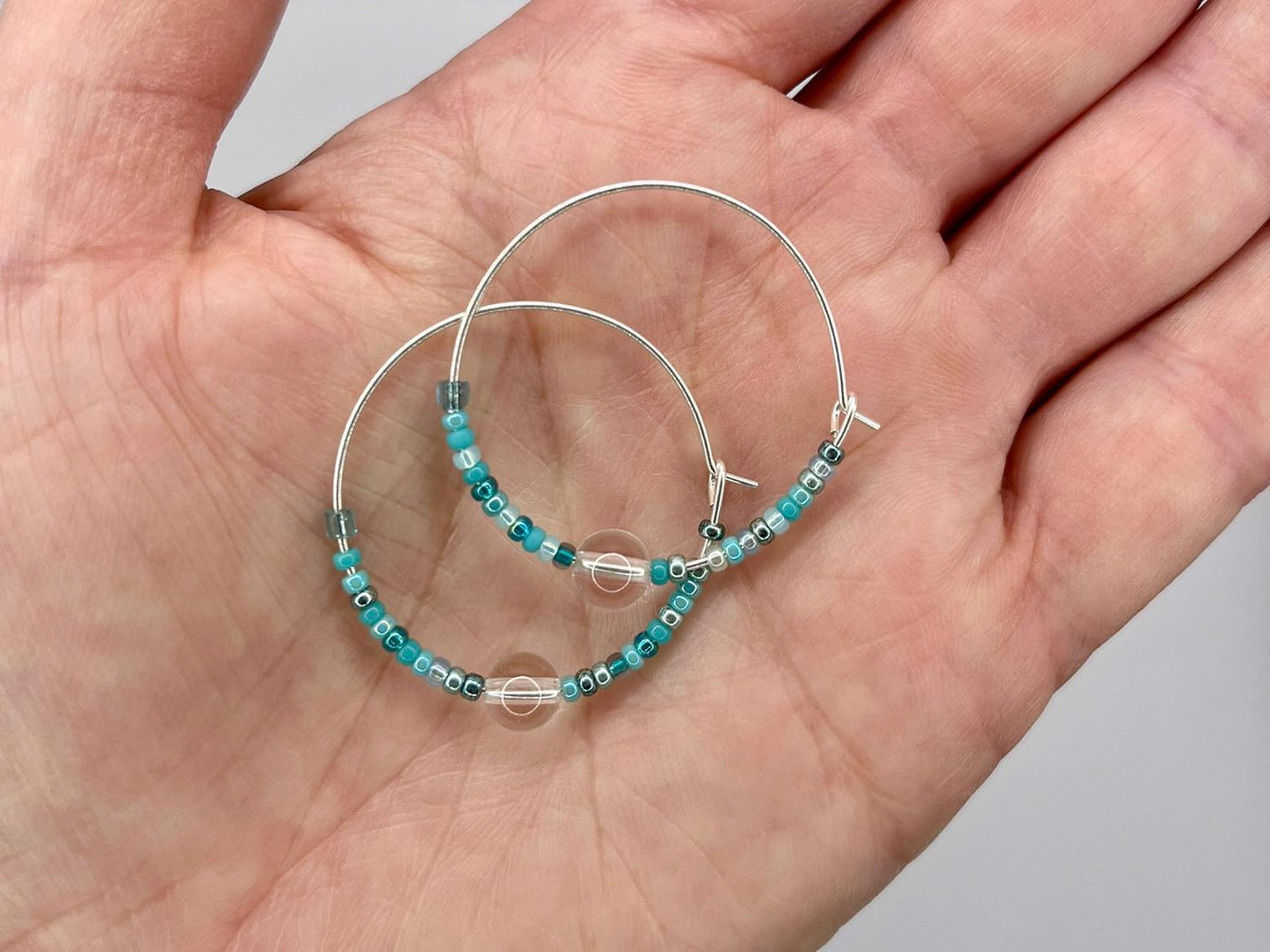 Pair of hoop earrings with turquoise beads held in a hand against a neutral background