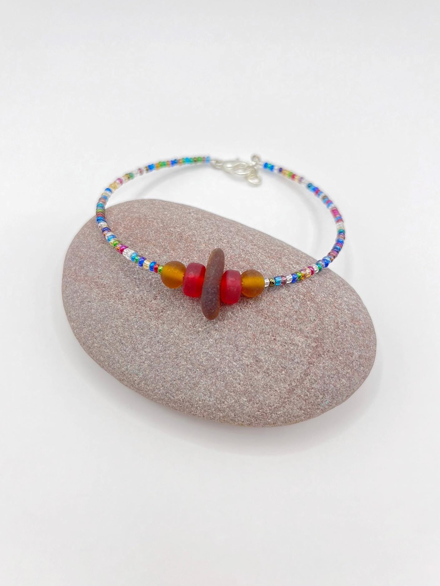 Rainbow beaded bracelet with sea glass and frosted glass beads laid on a purple pebble