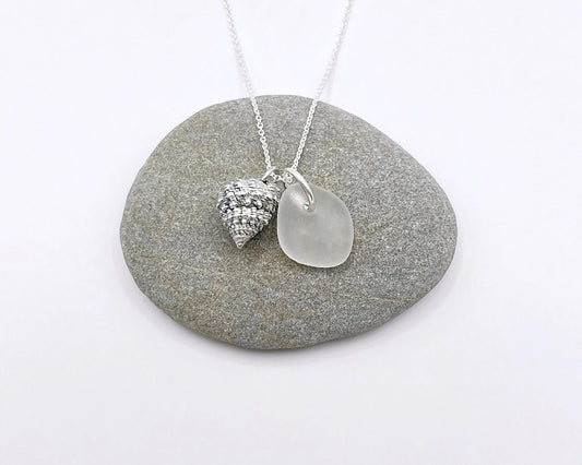 Silver necklace with White Sea glass and silver shell pendant laid on a grey pebble against a white background