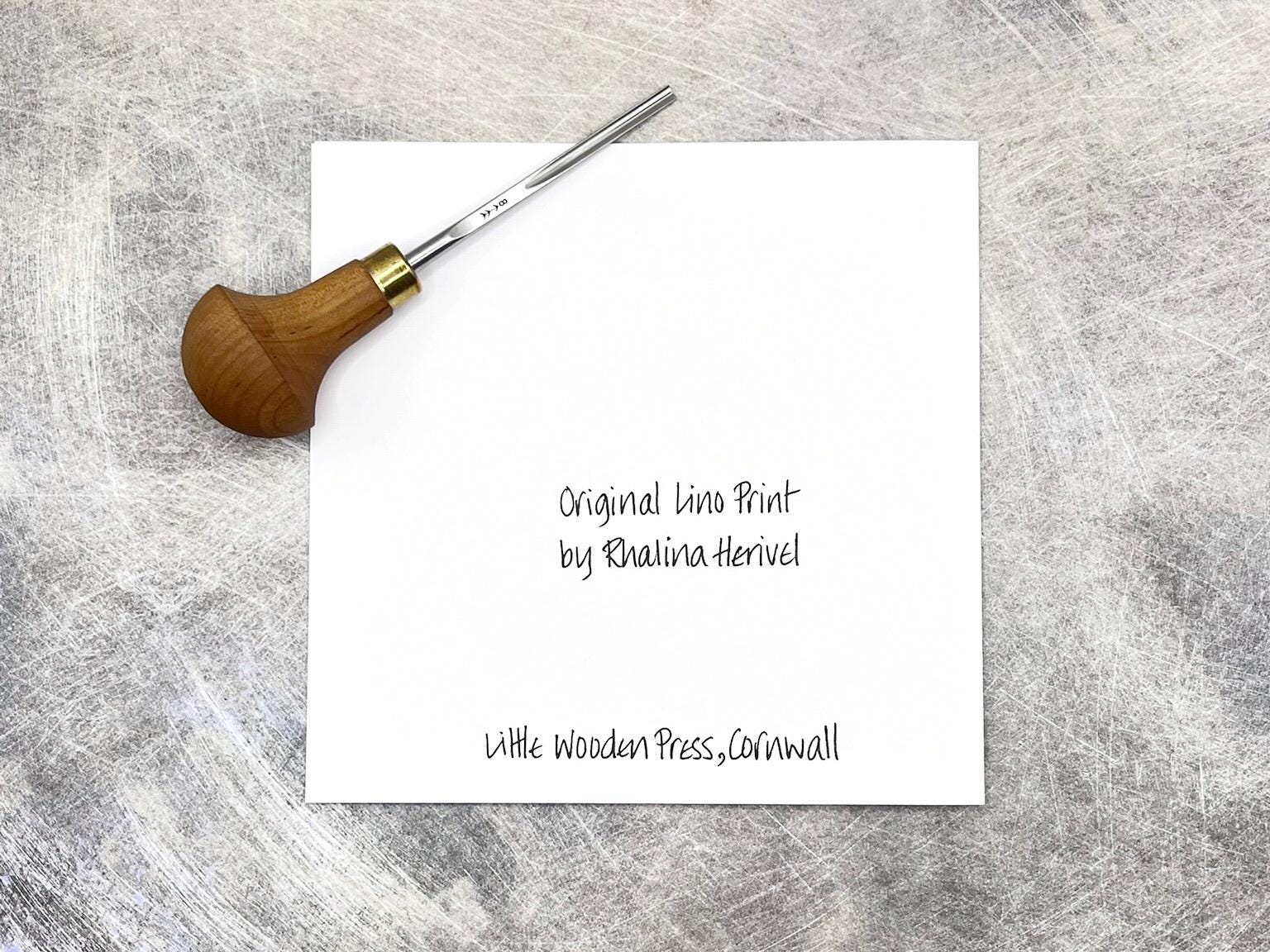 Showing the back of the card with text, laid on a textured surface. Photo includes lino cutting tool used