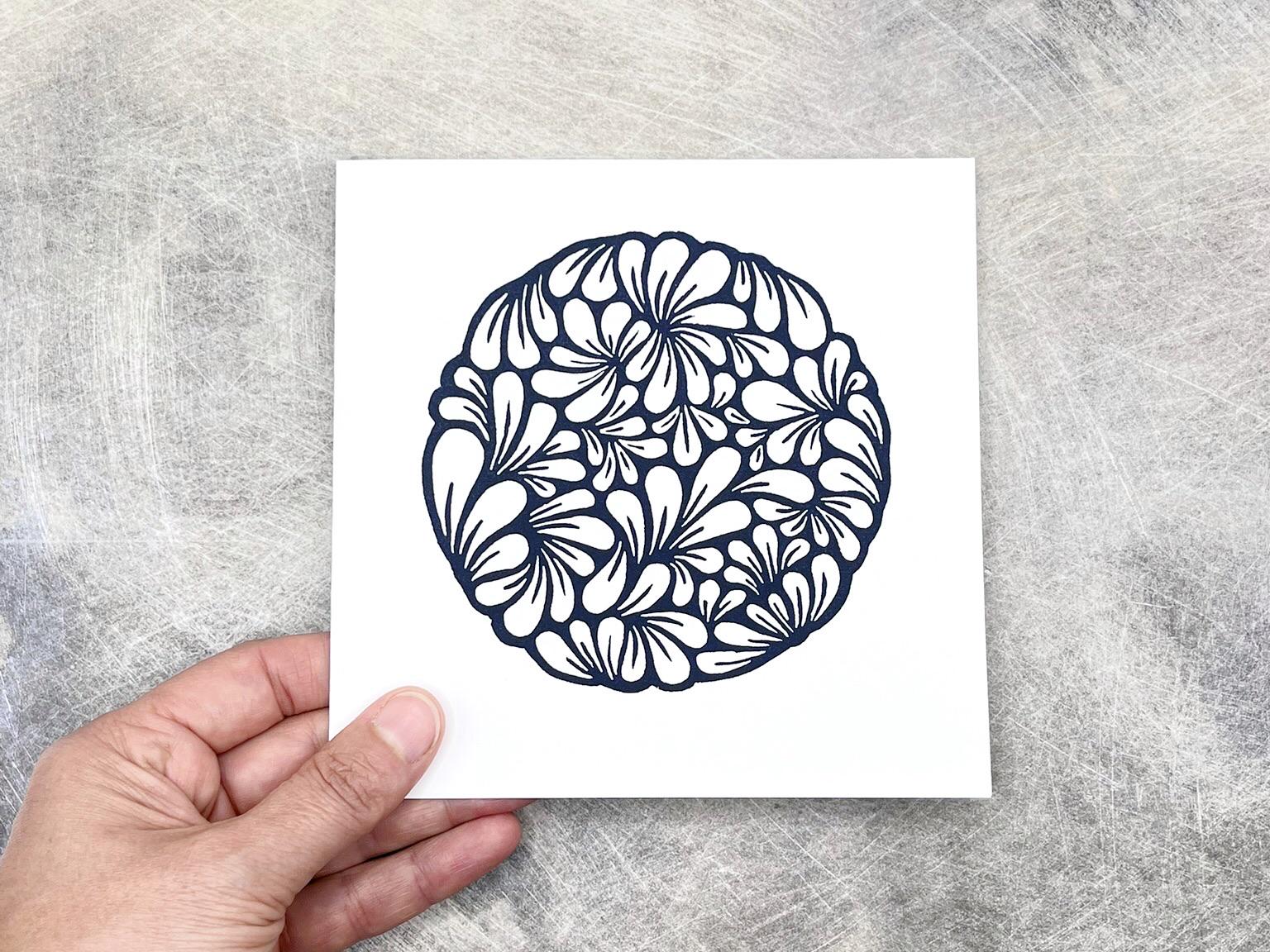hand holding original navy blue lino printed mussel shell pattern on white card against a textured background.