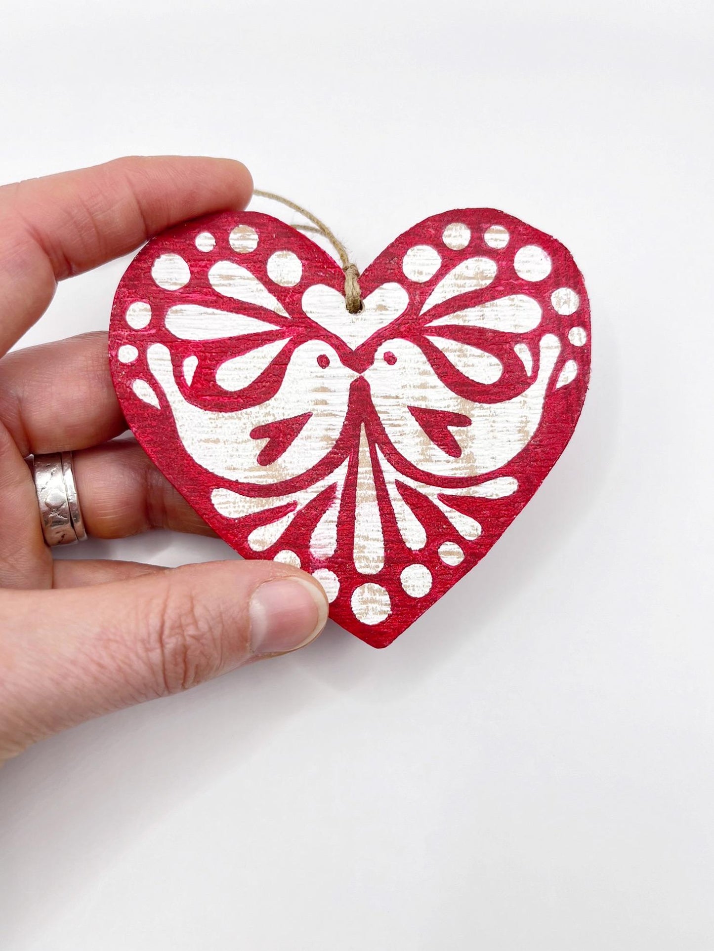 Red heart-shaped wooden hanging decoration with folk style love bird print   held in a hand against a white background