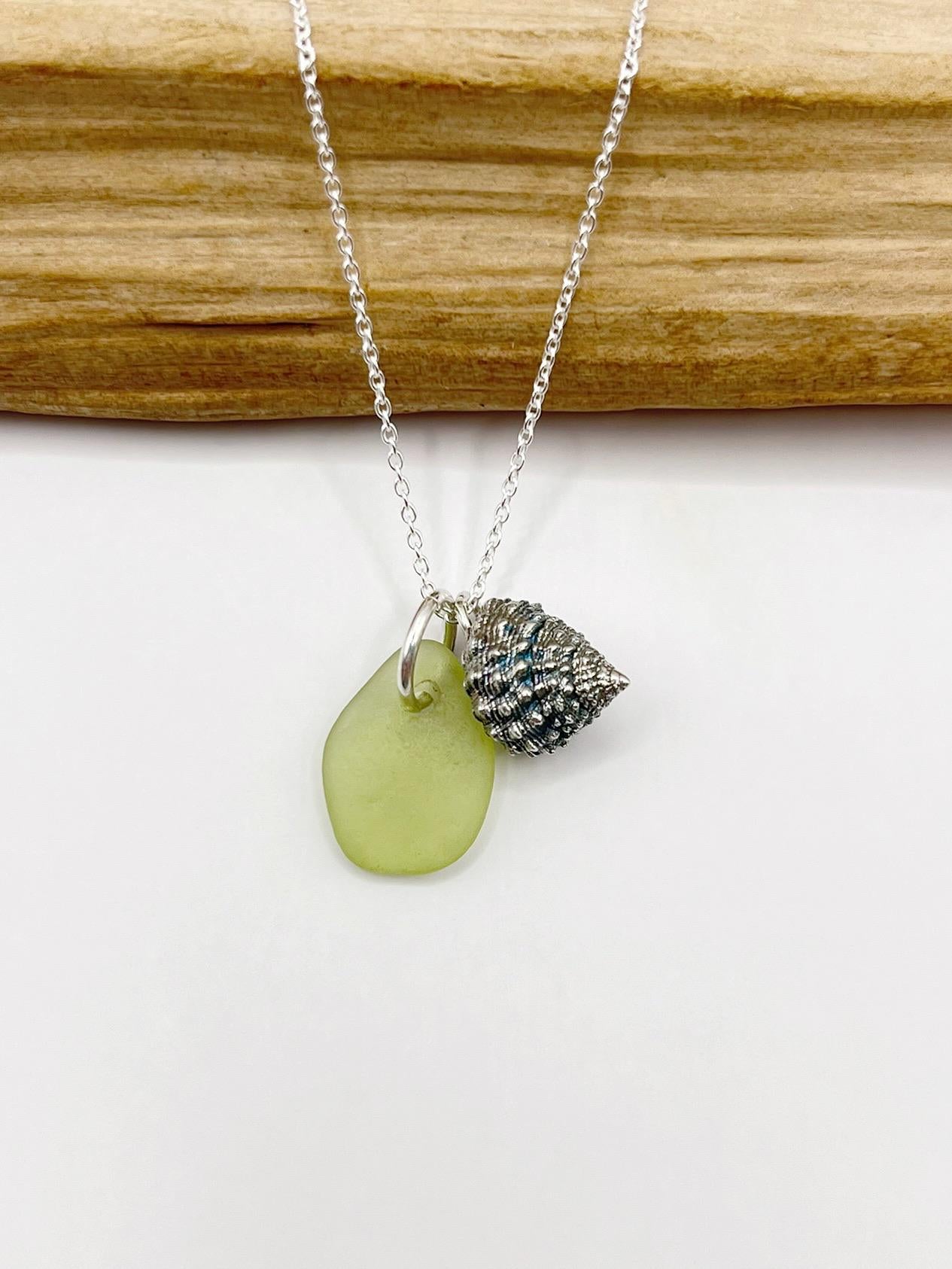Necklace with lime green sea glass and a silver shell charm laid on a white background