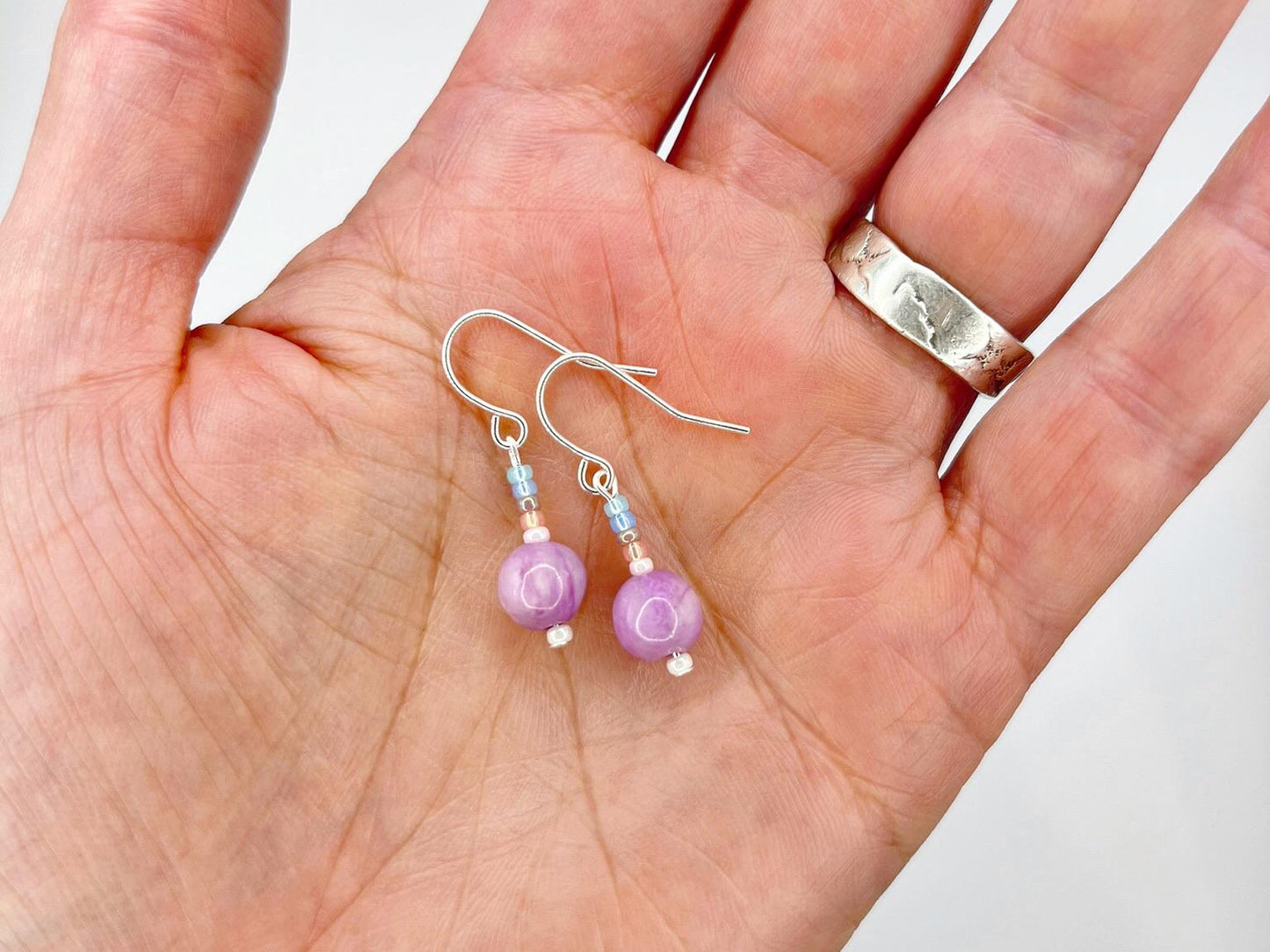 Pair of pastel seed bead and lilac jasper earrings held in a hand against a white background.