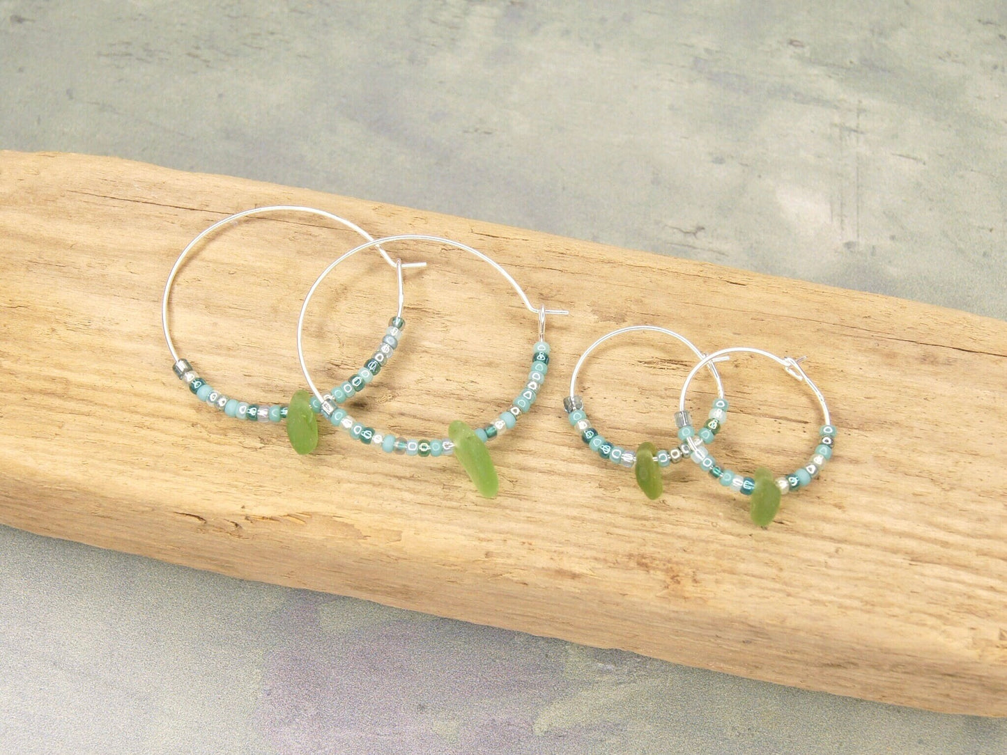 Turquoise seed bead hoop earrings with green sea glass laid on driftwood.