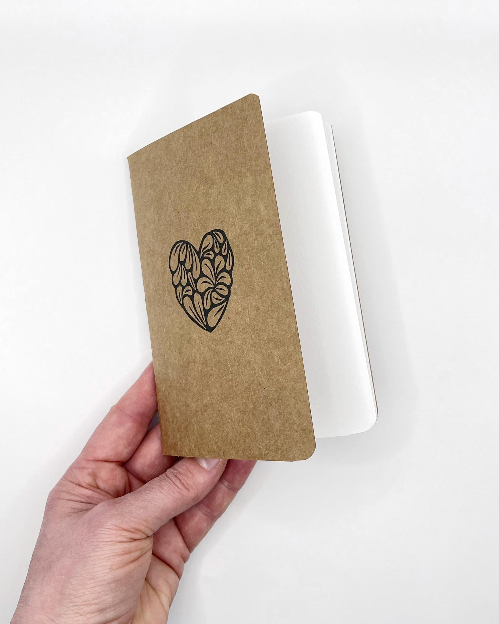 Hand holding a brown notebook with a black heart design on a white background